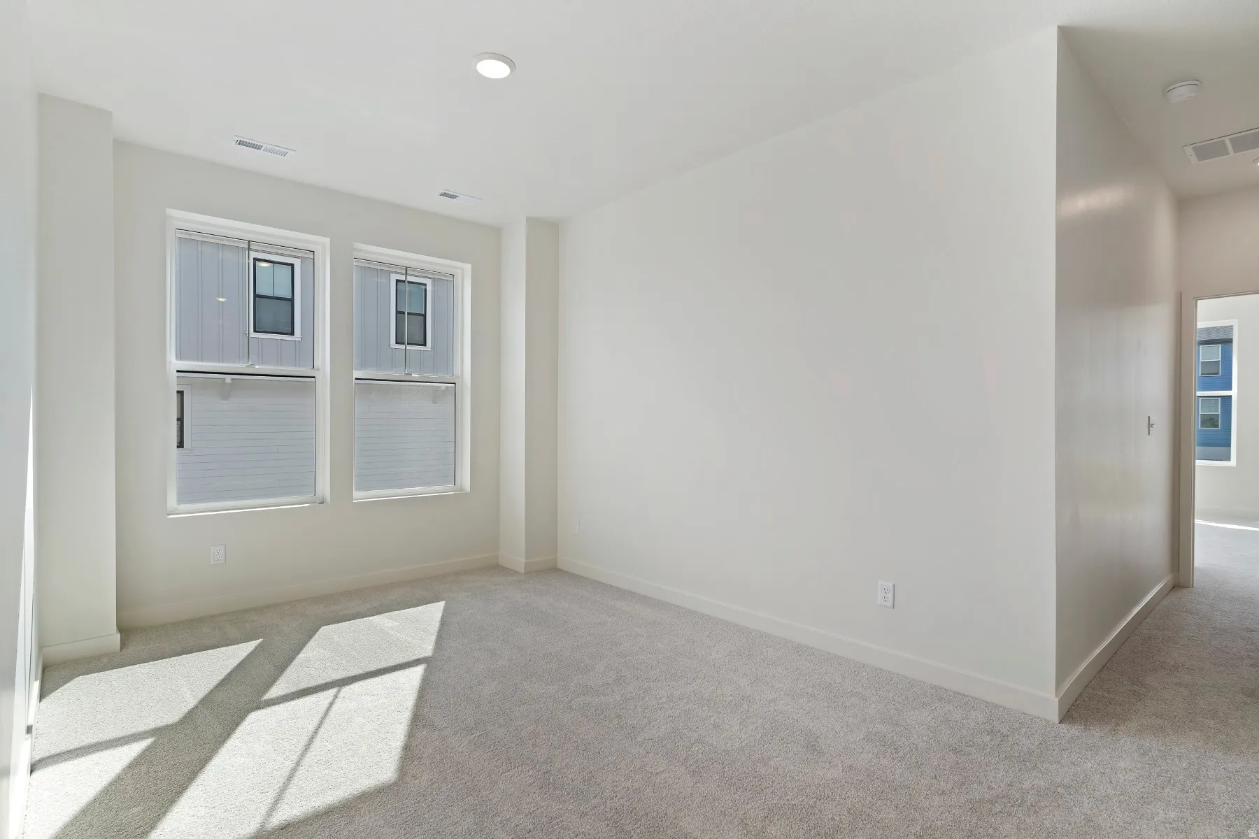 Spacious room with light gray carpet flooring, recessed lighting, and dual vertical windows