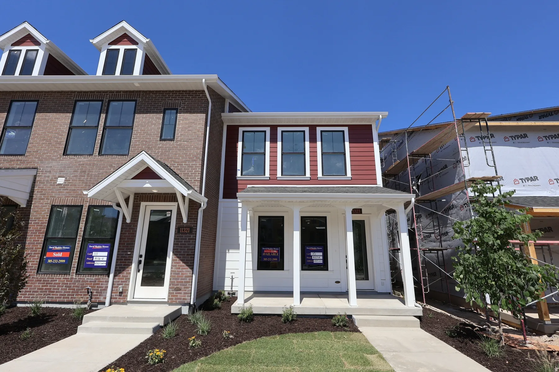 New construction home featuring a red siding facade with white trim, a covered front porch with white columns, and a landscaped front yard with a concrete walkway