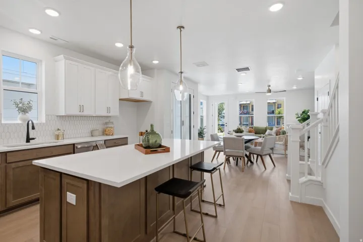 Open-concept living area featuring a kitchen island with seating, pendant lighting, wood-finish flooring, and white cabinetry