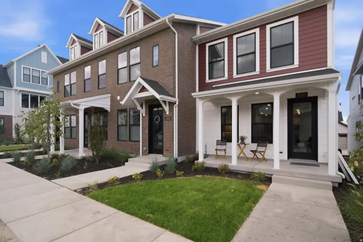 Contemporary townhome facade featuring a covered front porch, dark-framed windows, and white trim