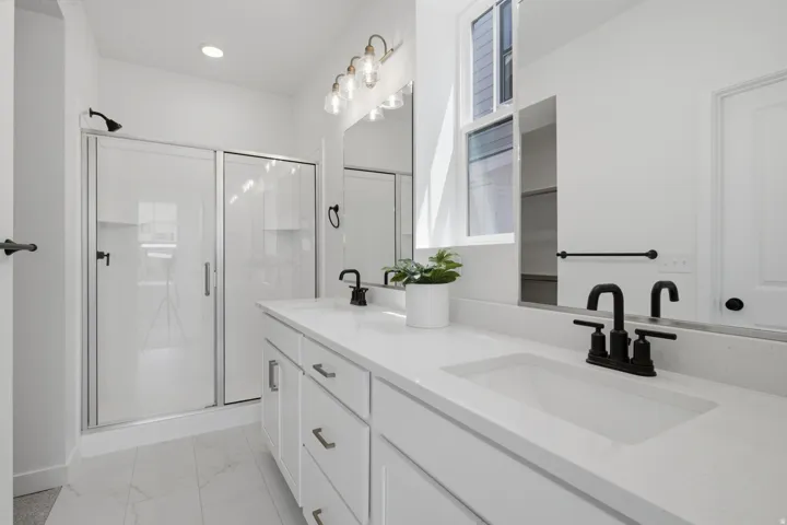 Primary bathroom with dual vanities, quartz countertops with integrated sinks, white cabinetry, and matte black fixtures