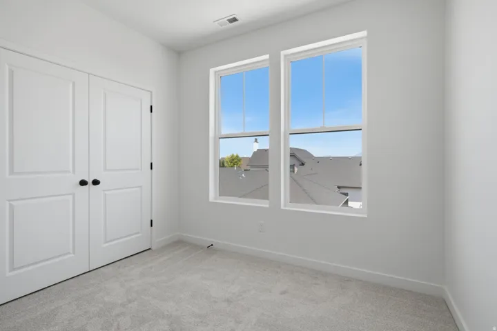 Bright secondary bedroom featuring large double-hung windows with white frames, neutral carpeting, and clean white walls