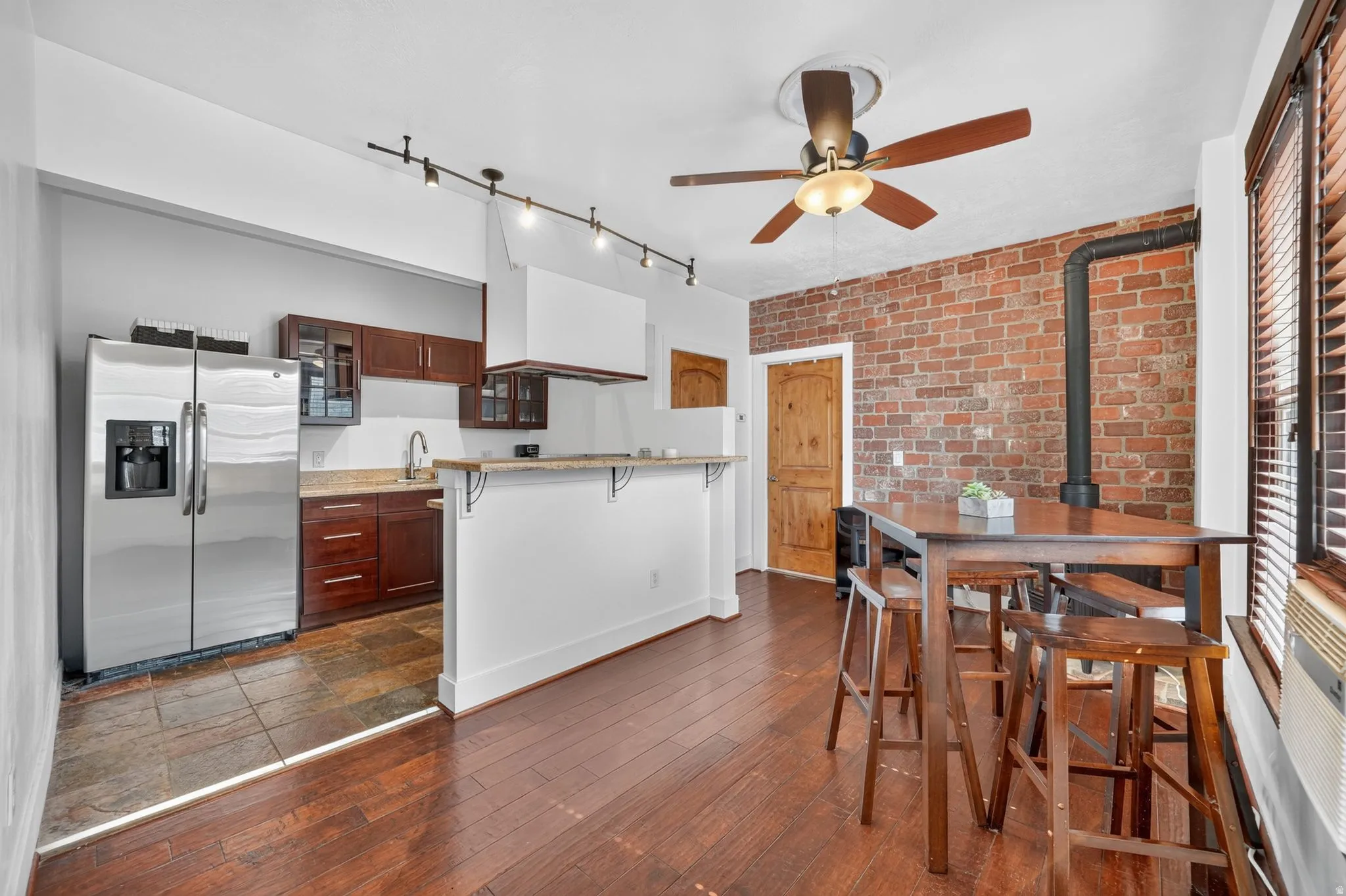 Open-concept living space featuring laminate flooring, an exposed brick accent wall, and a ceiling fan