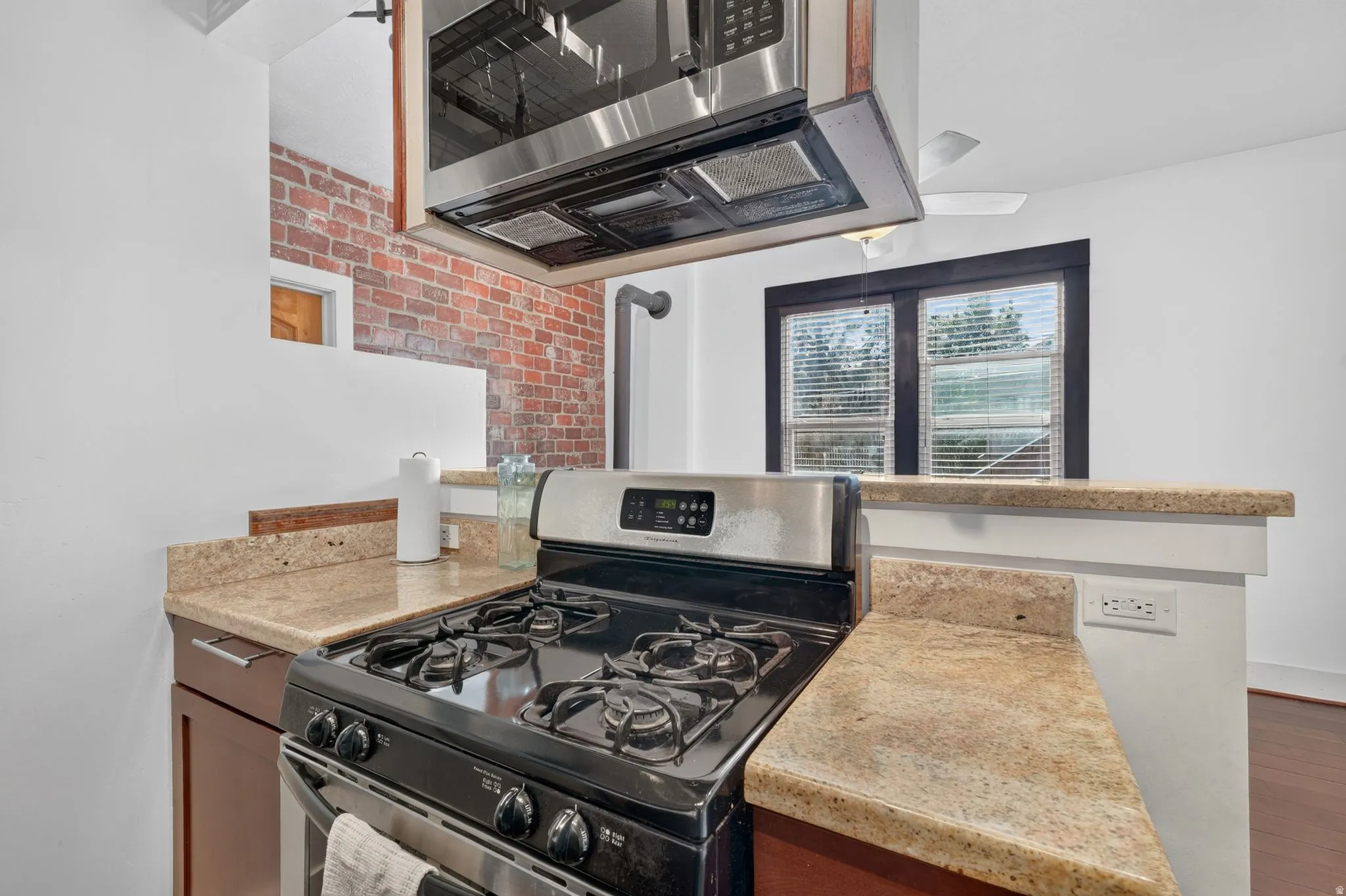 Kitchen featuring granite-style countertops, stainless steel appliances, a built-in microwave, and exposed brick accents