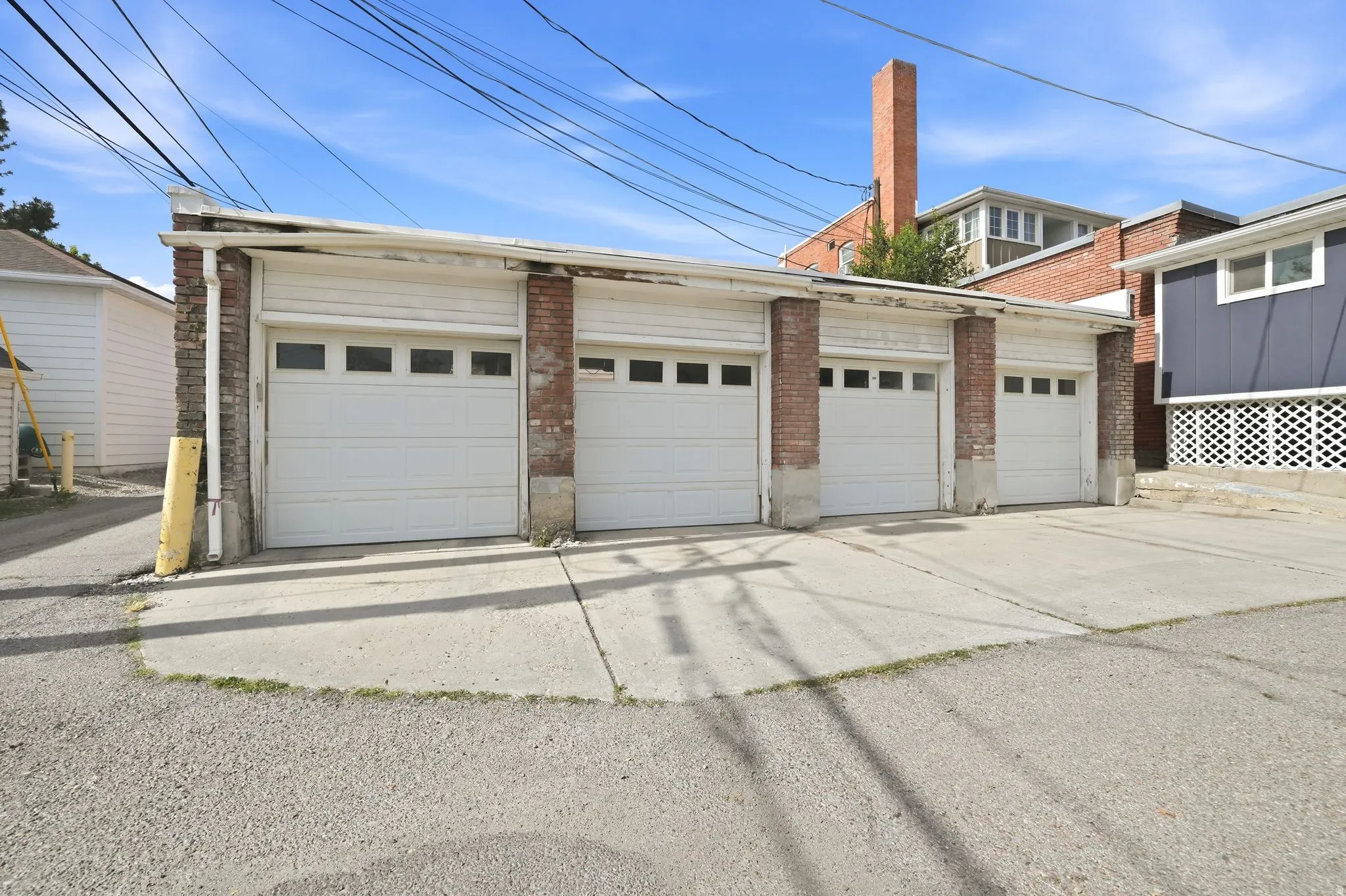 Four-bay garage structure featuring white panel garage doors with window inserts, brick pillar accents, and a concrete driveway apron