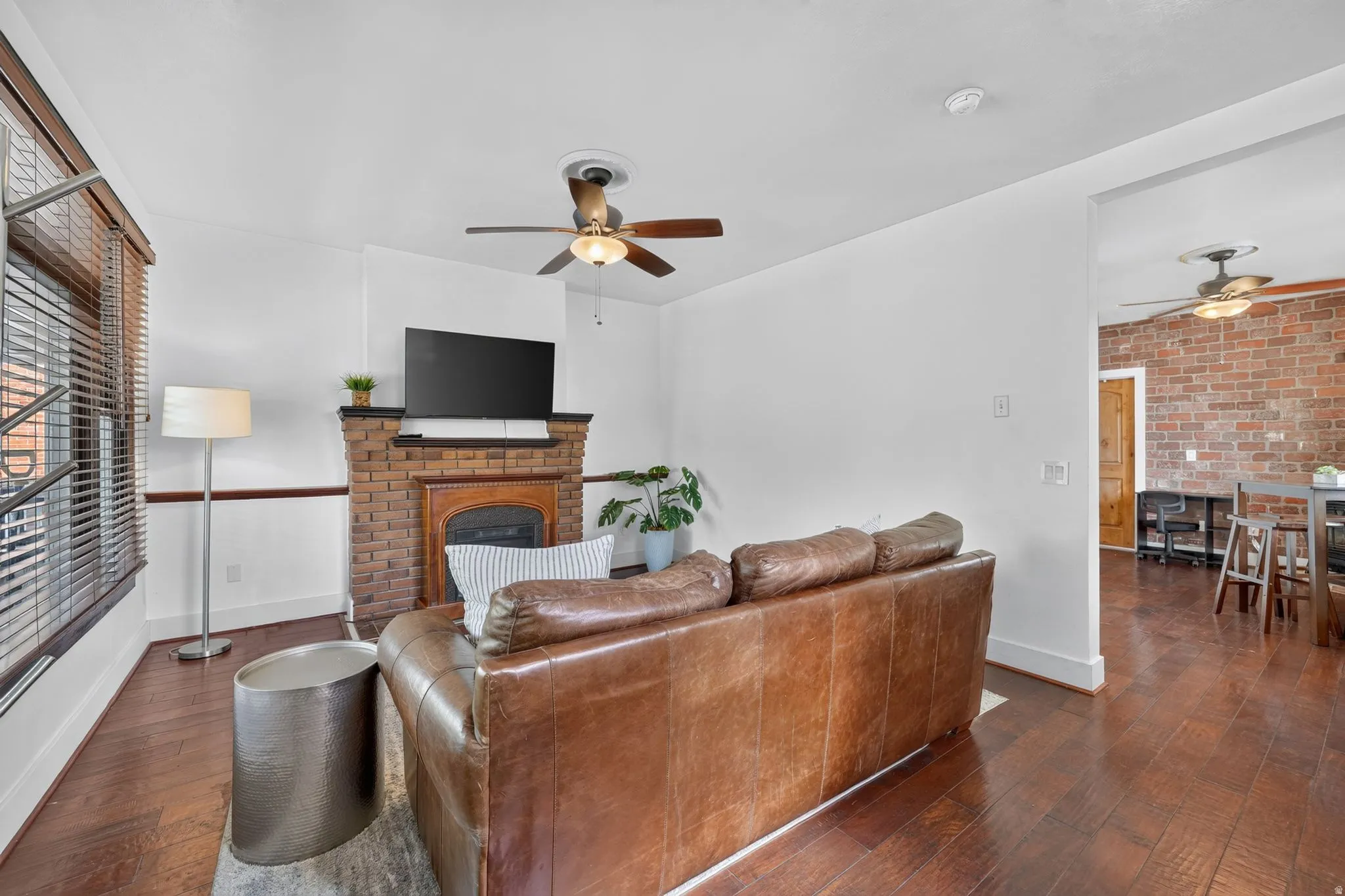 Living area featuring laminate flooring, a brick fireplace with a wood mantel, and a ceiling fan