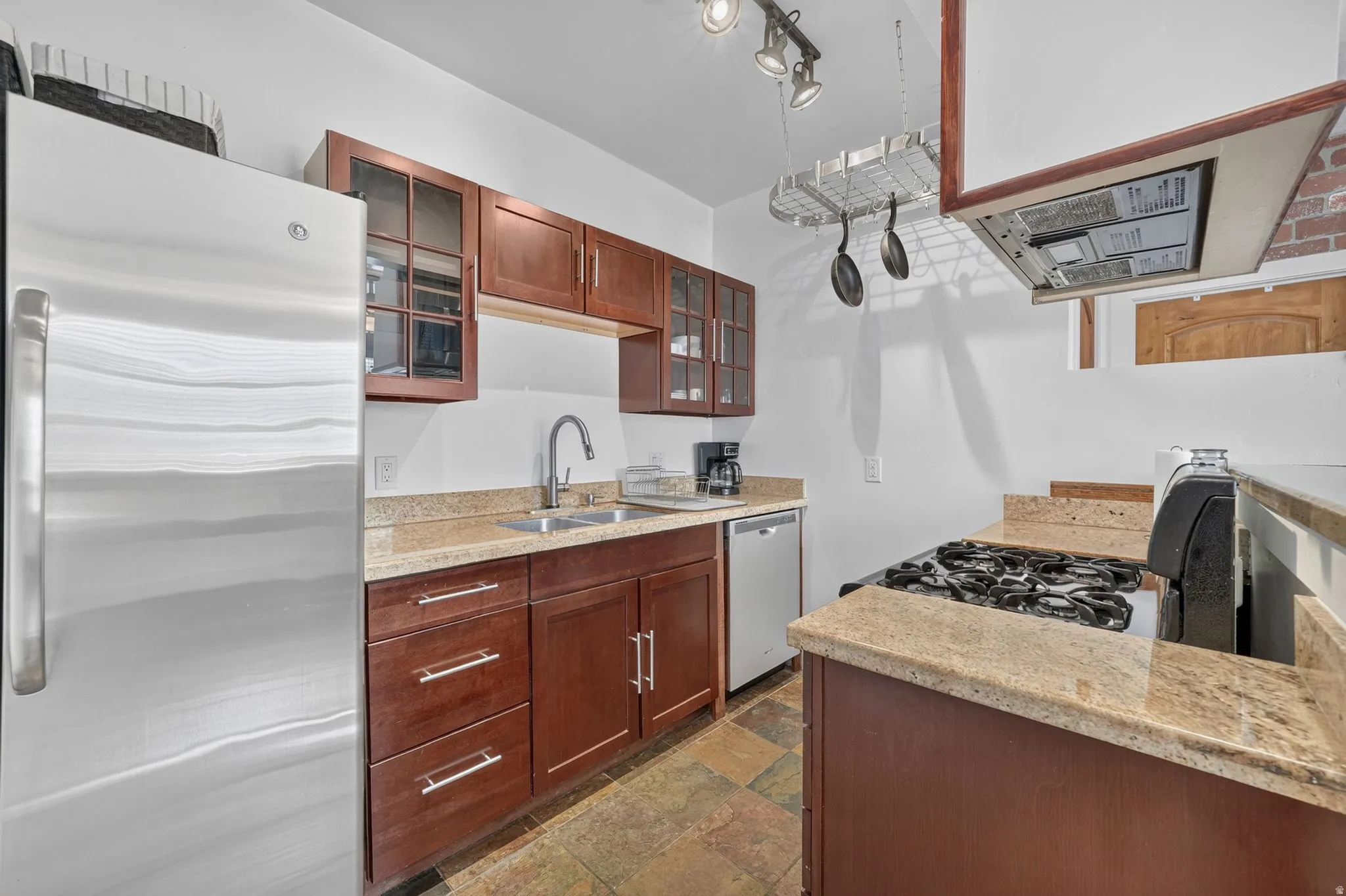 Kitchen featuring stainless steel appliances, wood cabinetry with glass-front uppers, light-toned countertops, and multi-tone floor tiling