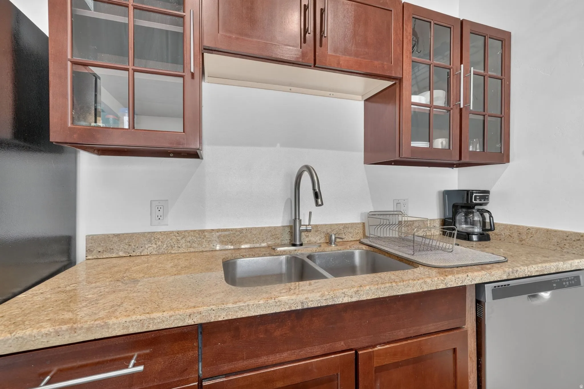Kitchen featuring a double basin stainless steel sink with a gooseneck faucet, light granite-style countertops, wood cabinetry with glass-front uppers, and an integrated dishwasher