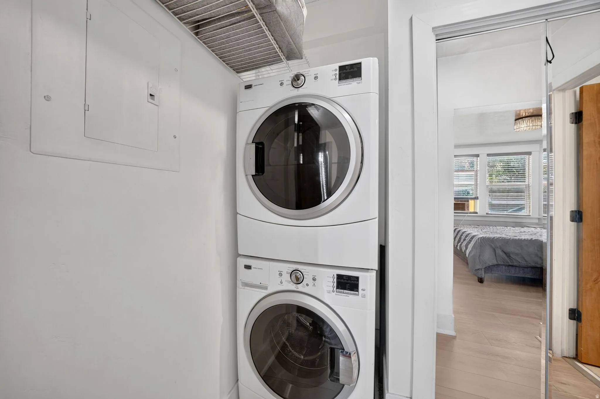 Integrated laundry area featuring a stacked washer and dryer, adjacent to a room with light wood-finish flooring and multiple windows