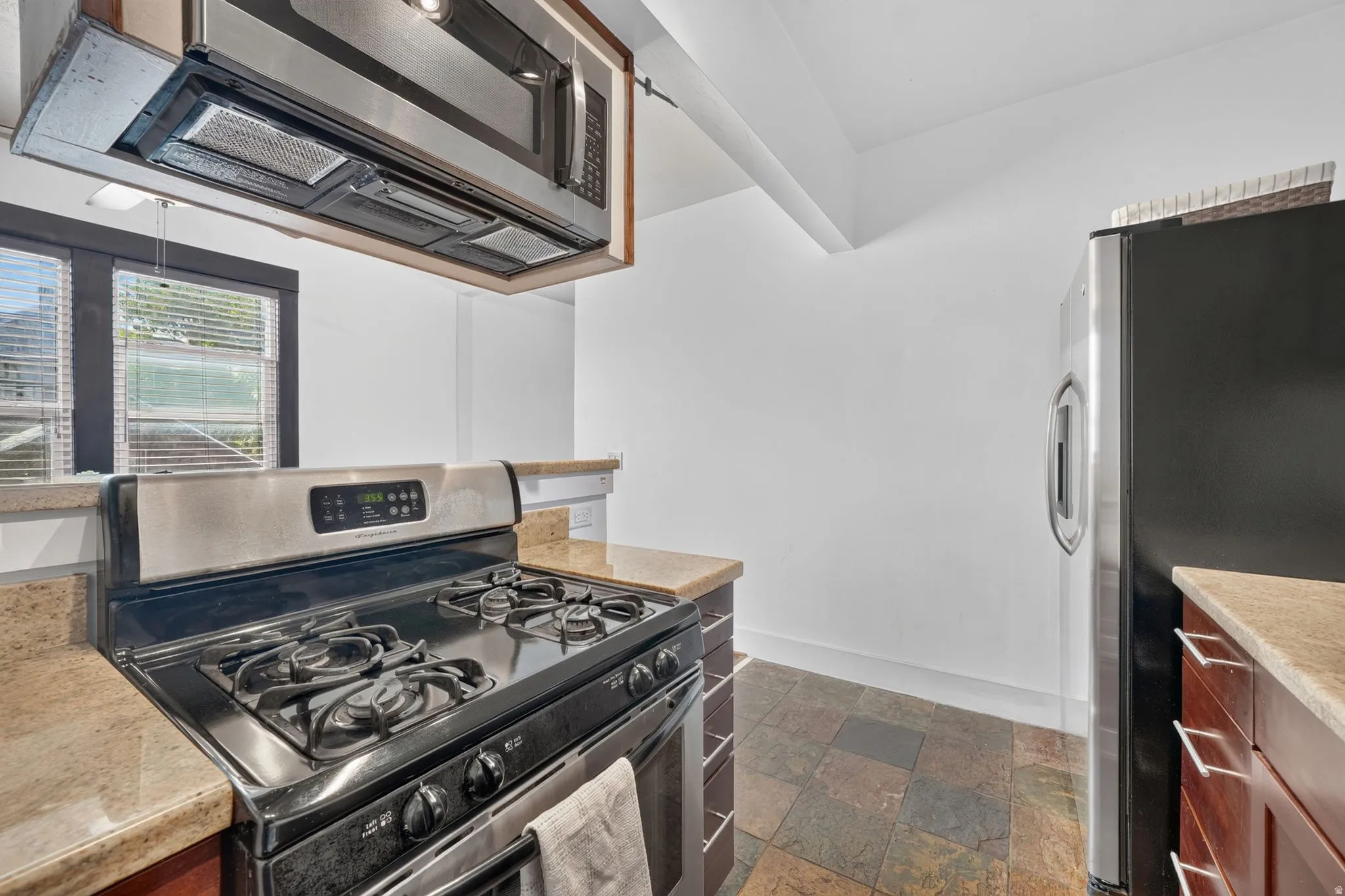 Kitchen featuring a stainless steel range with overhead microwave, stone-finish countertops, wood cabinetry, and slate tile flooring