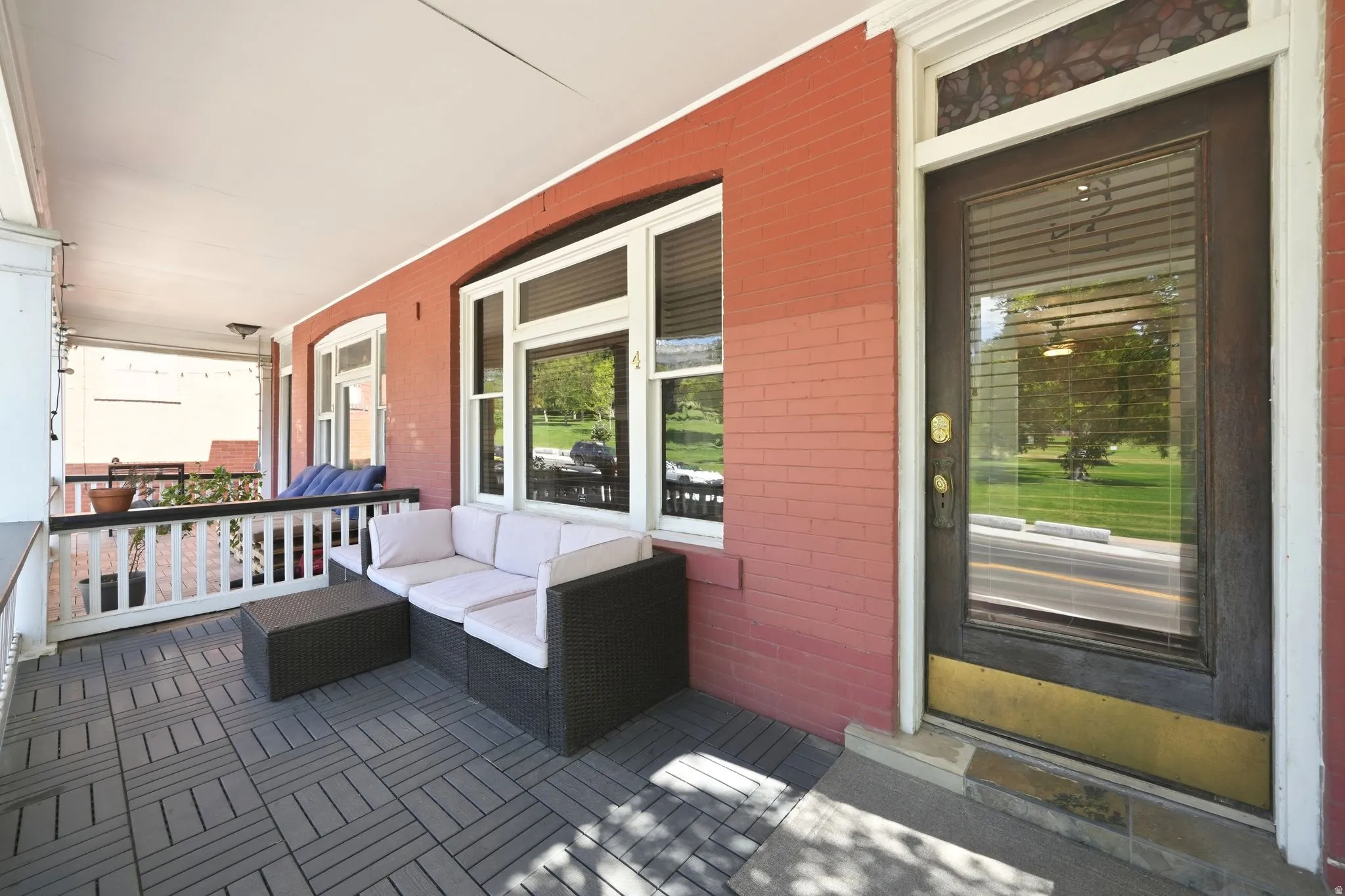 Covered front porch featuring brick siding, white trim, and a dark-paneled entry door with an upper stained glass transom