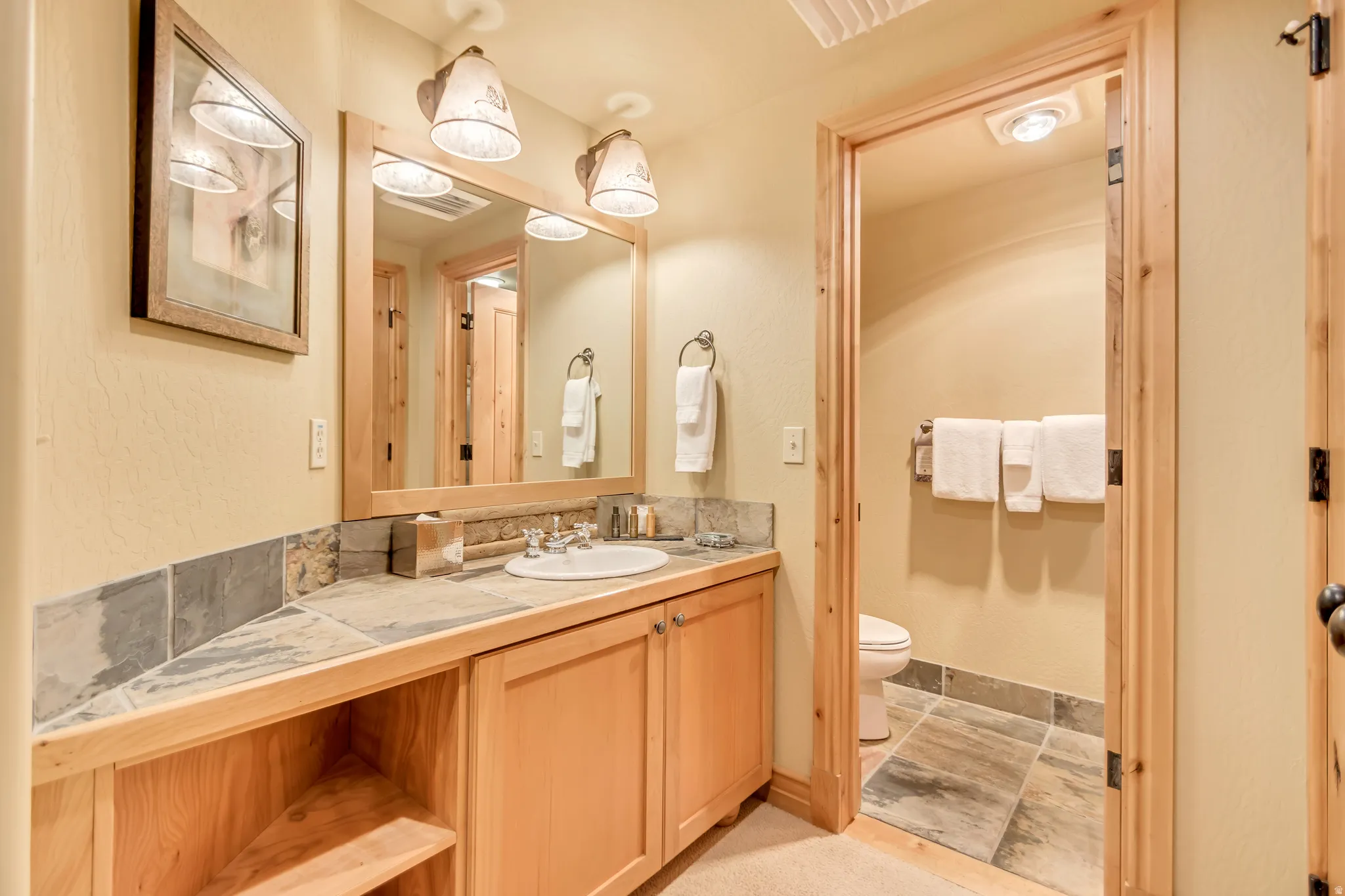 Bathroom vanity with a built-in sink, wood-finish cabinetry, and a stone tile countertop