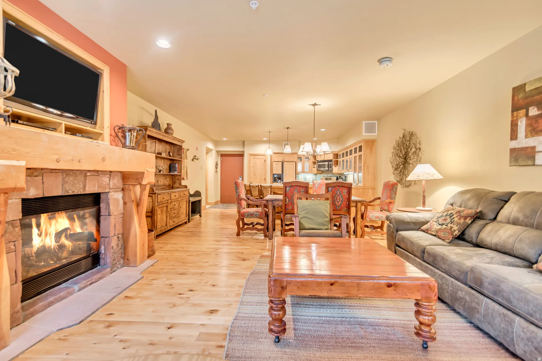 Open-concept living area featuring light wood-finish flooring, a stone and wood fireplace, recessed lighting, and a dining area with pendant lighting
