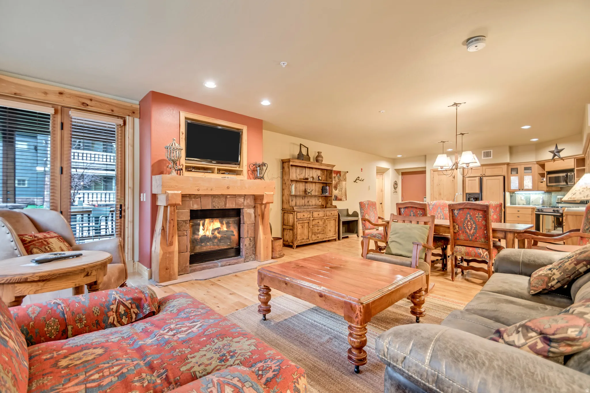 Living area featuring a stone fireplace with a wood mantle, wood-finish flooring, and a balcony access door