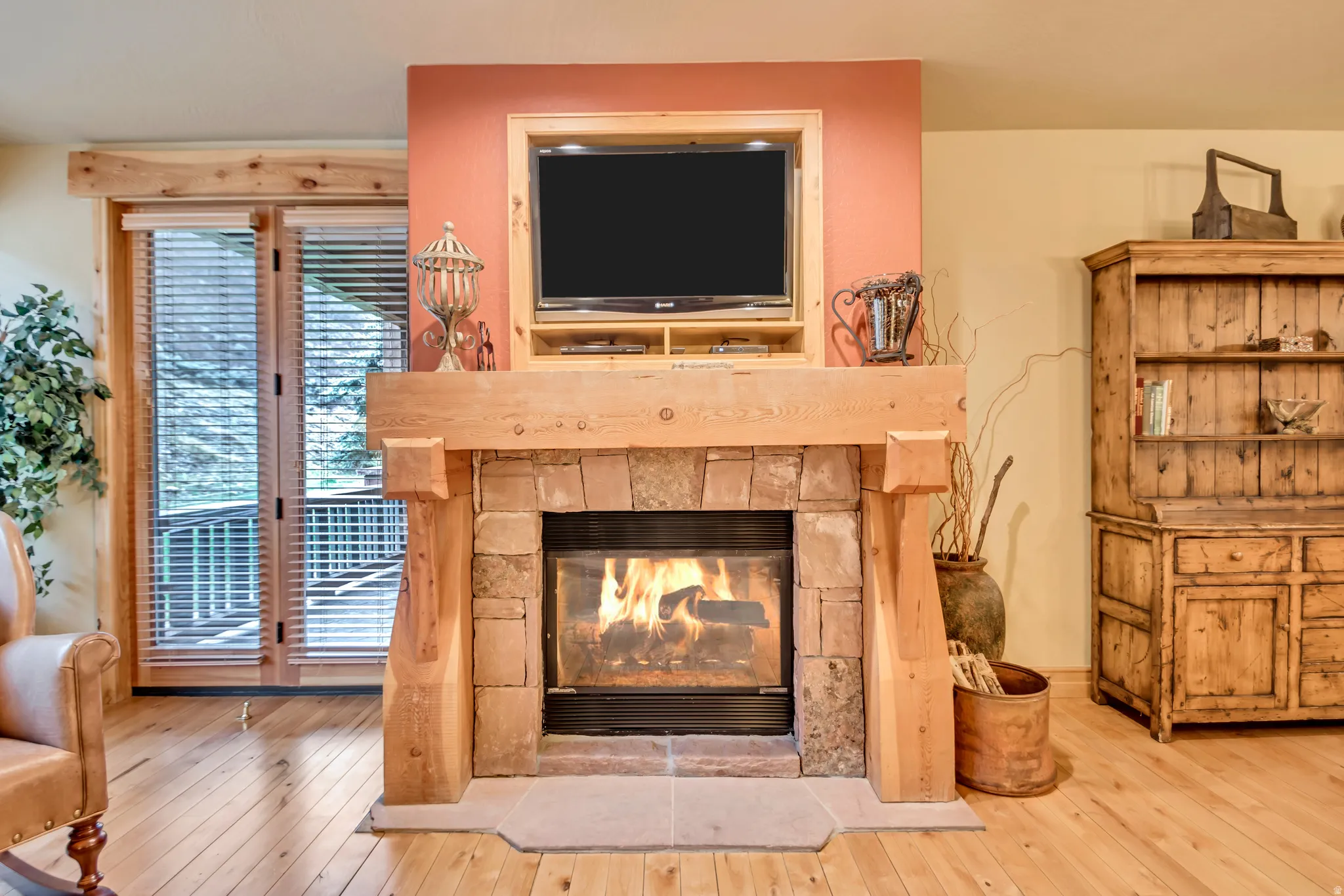 Stone-clad fireplace with a substantial wood mantel, wood-finish flooring, and double French doors with blinds