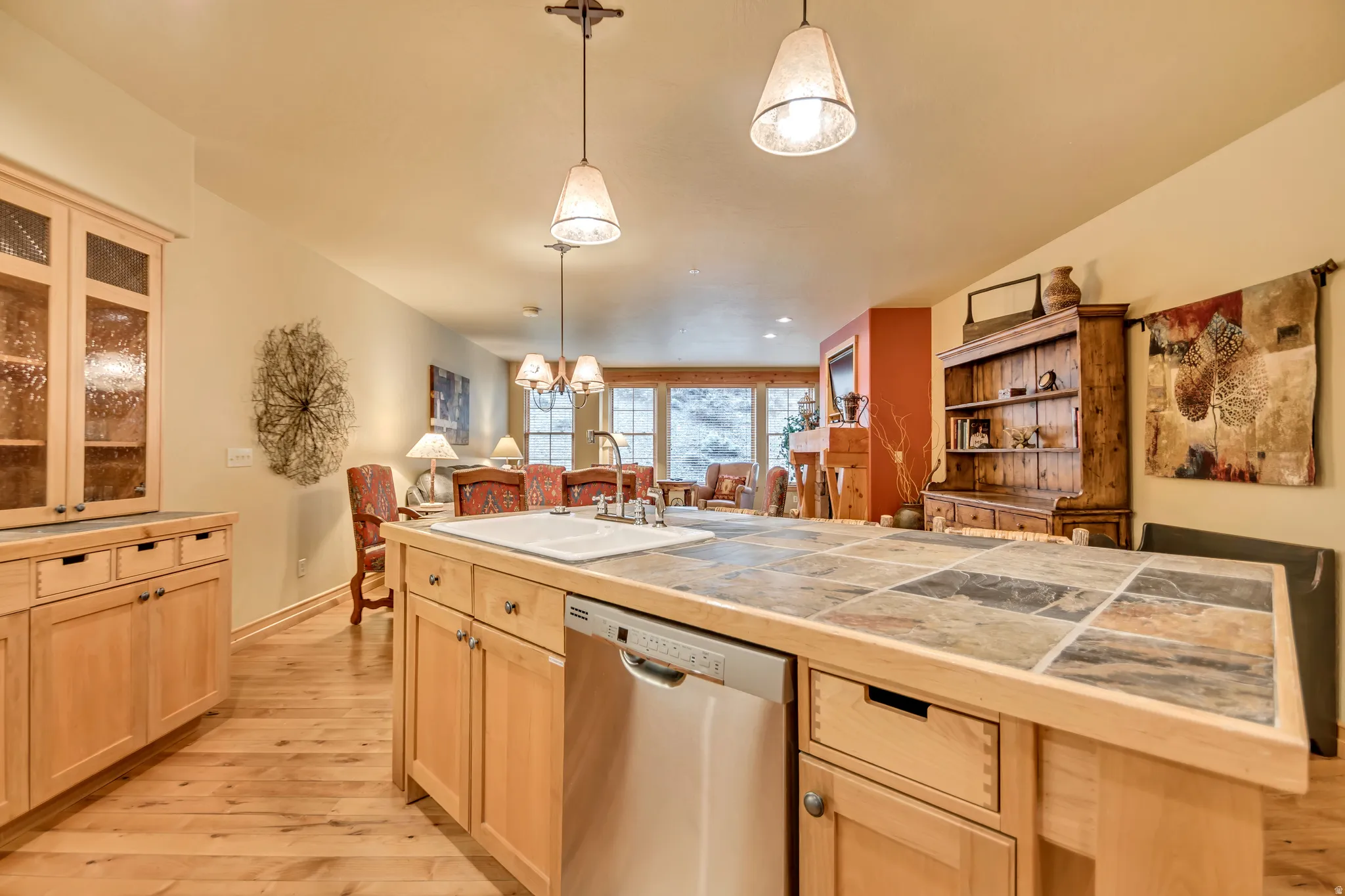 Kitchen featuring light wood cabinetry, a tiled island countertop with an integrated sink and stainless steel dishwasher, and wood-finish flooring