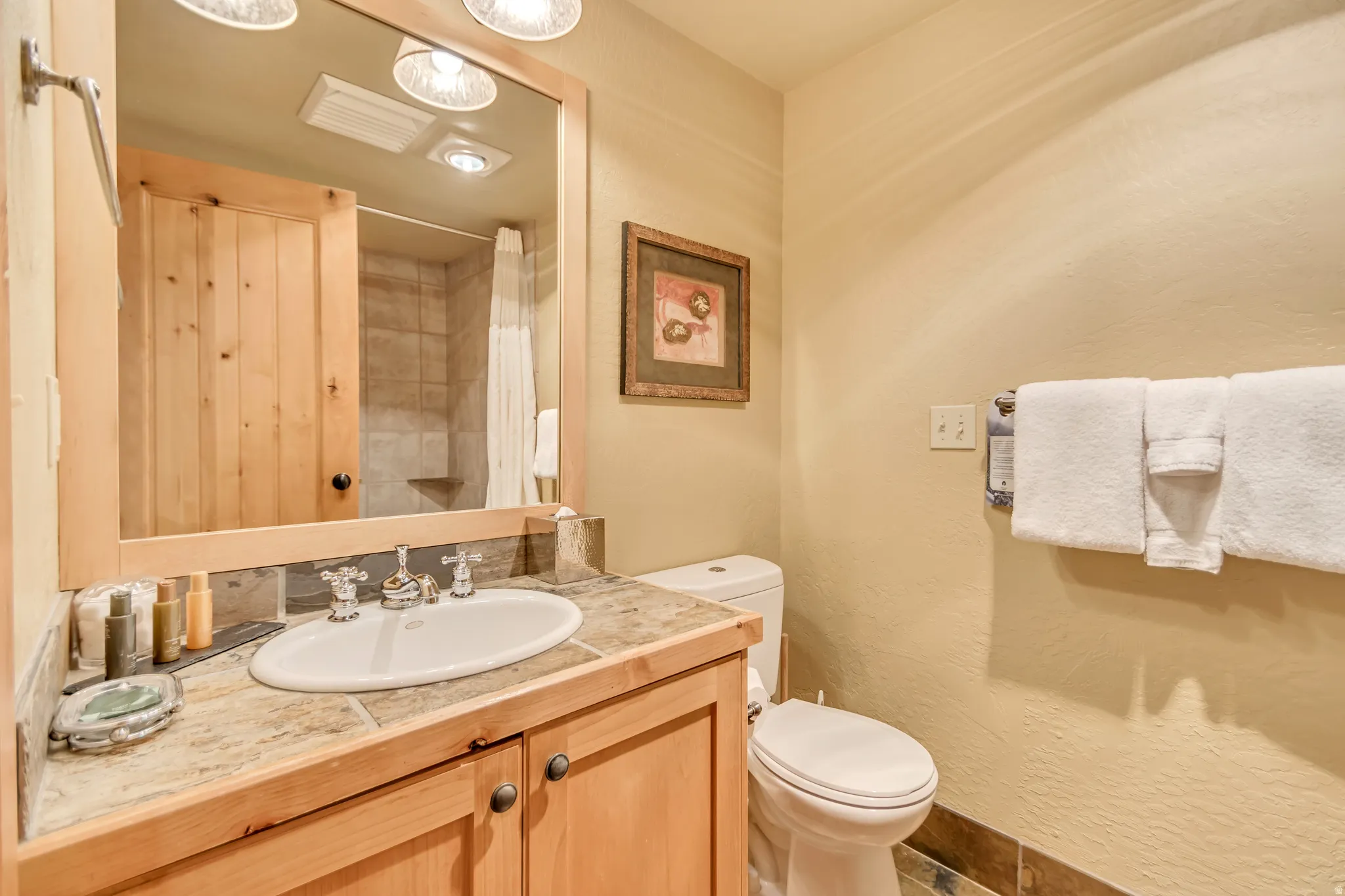 Bathroom featuring a light wood-finish vanity with an integrated sink, natural stone countertop, and decorative mirror
