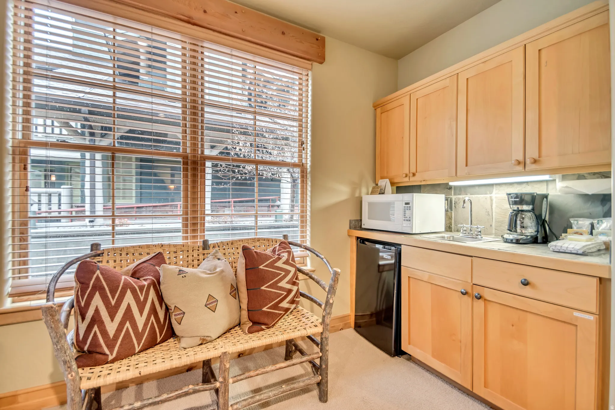 Compact kitchenette featuring light wood cabinetry, stone-look countertops, and a tiled backsplash