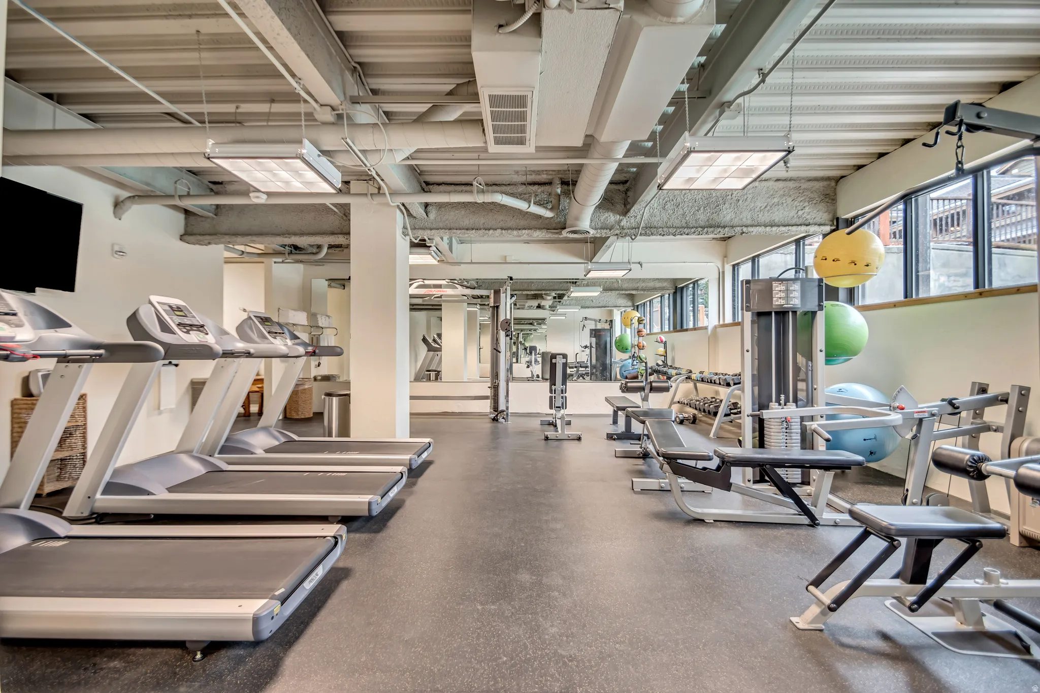 Fitness center featuring rubber flooring, exposed ceiling ducts, recessed lighting, expansive windows, and a mirrored wall