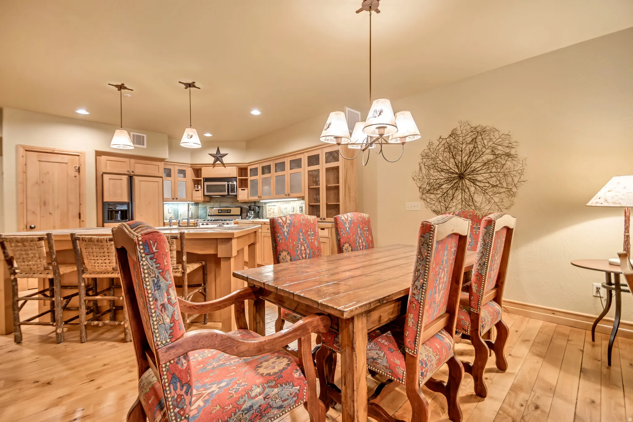 Open-concept dining area featuring wood-finish flooring, a wood dining table, and a kitchen with wood cabinetry, stainless steel appliances, and a breakfast bar with pendant lighting