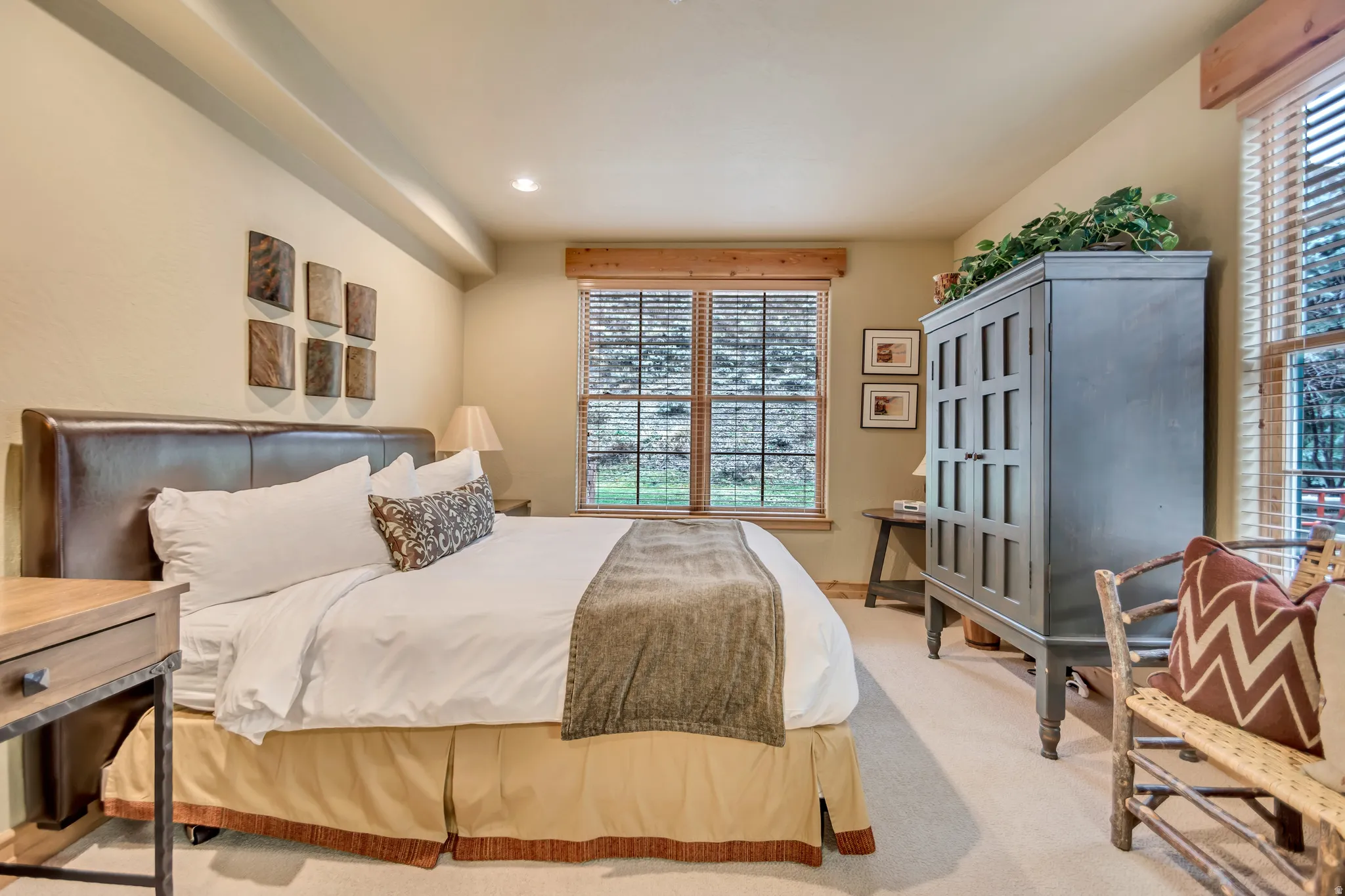 Carpeted bedroom with a dark leather-finish headboard and two windows featuring wood blinds