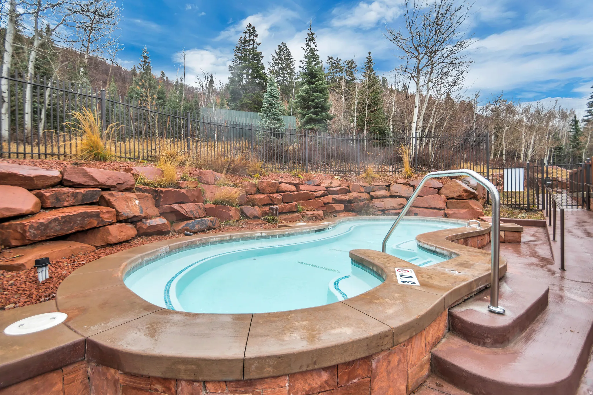 Outdoor spa with integrated steps, stainless steel handrails, and surrounding stone retaining walls