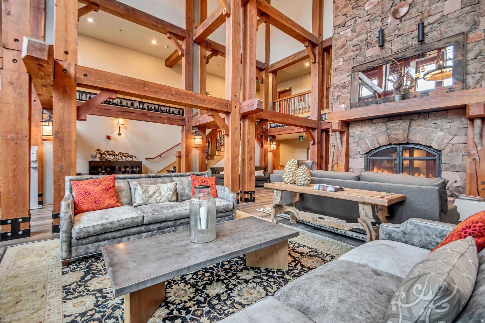 Expansive great room featuring a grand stone fireplace with a raised hearth, a prominent wood beam structure, and a patterned area rug