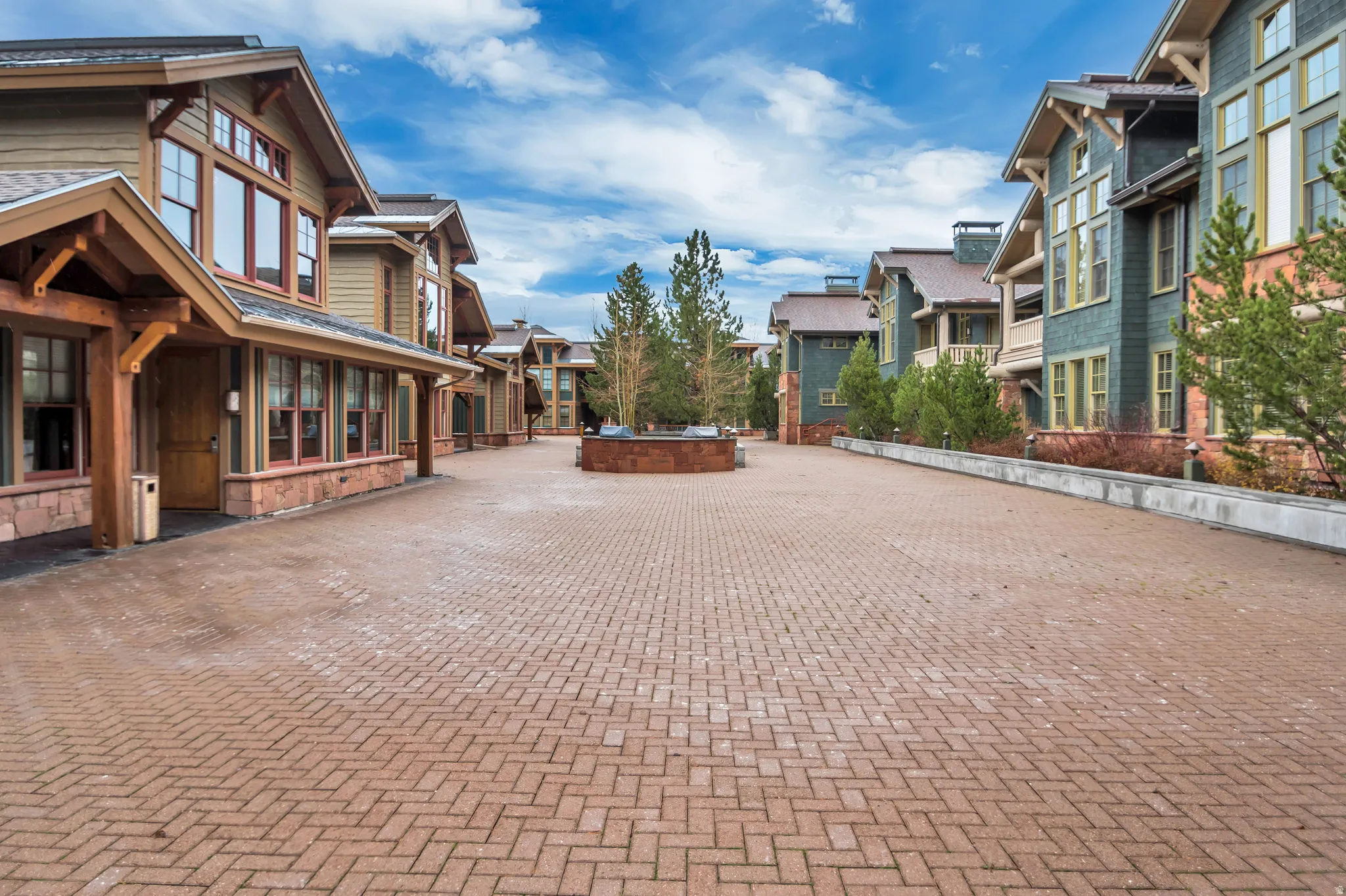 Expansive paver driveway leading to multiple residences featuring craftsman-style architecture, wood siding, large windows, and stone accents