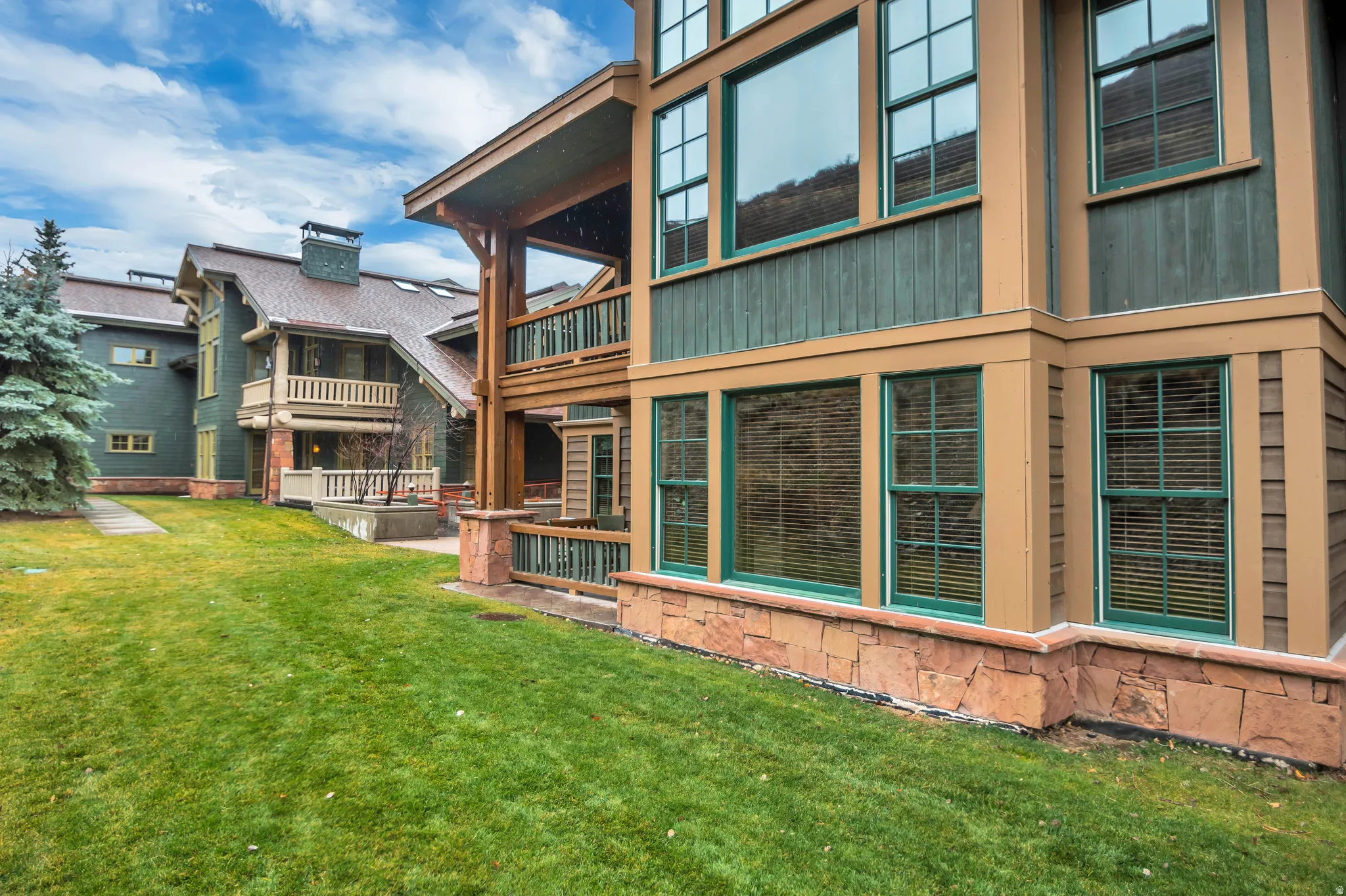 Exterior featuring multi-level architecture with stone and wood siding, green window frames, and multiple balconies