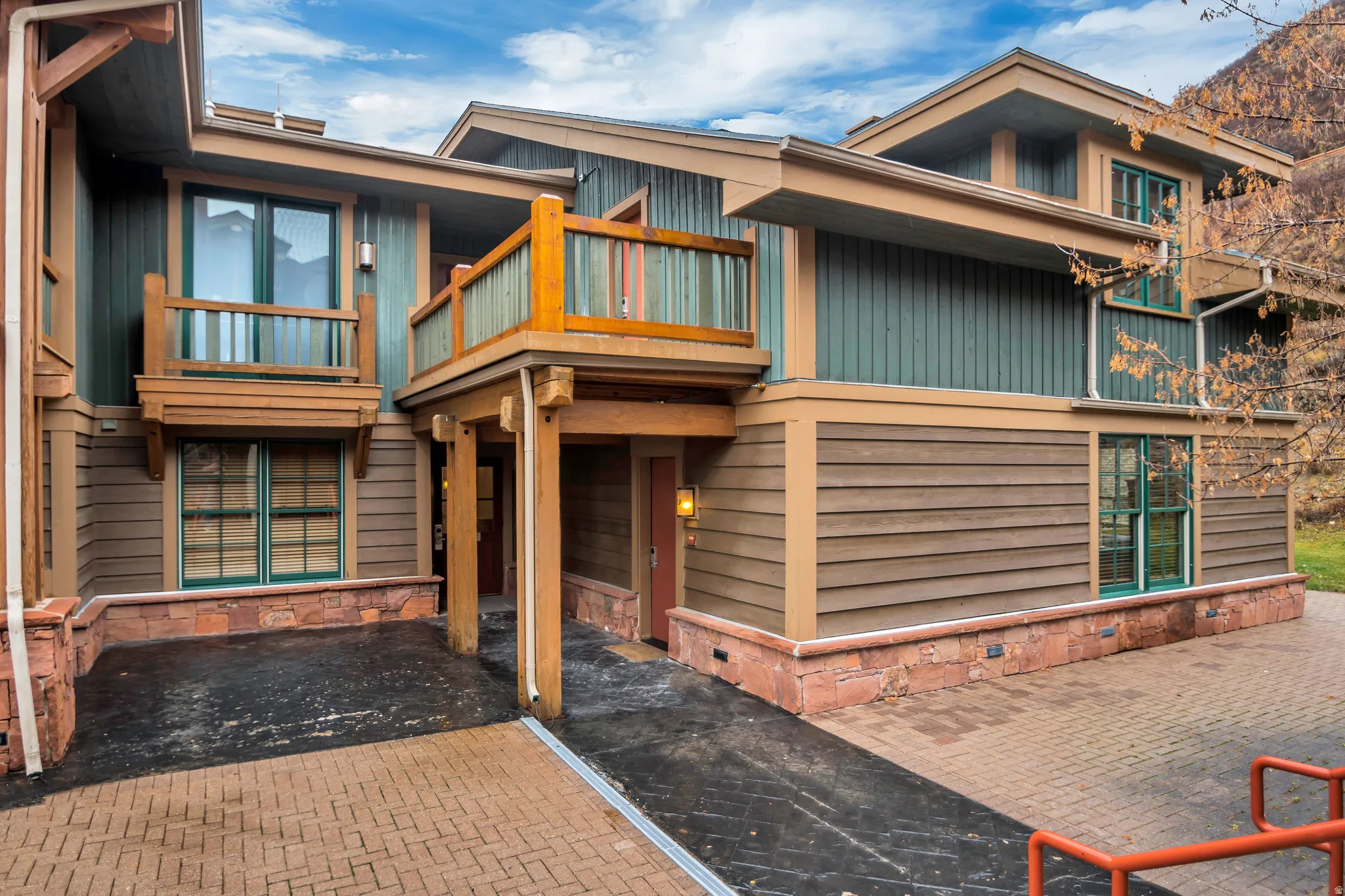 Multi-level exterior featuring wood-tone siding, green vertical paneling, stone base, and green window frames