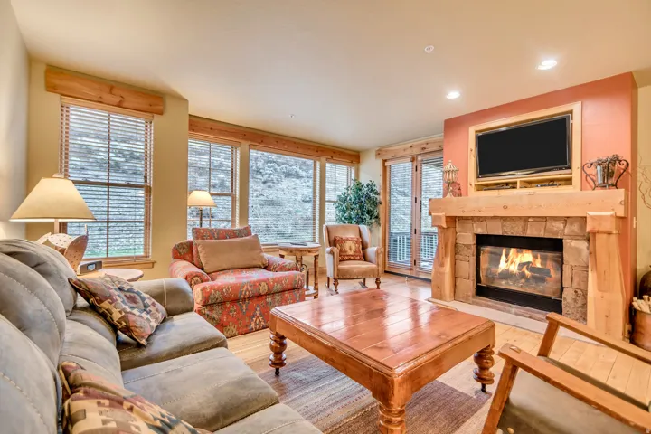 Living area featuring wood-finish flooring, a stone-surround fireplace with a wood mantle, and multiple windows providing natural light