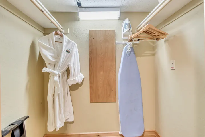 Compact utility closet featuring a wall-mounted ironing board, integrated hanging rods, and a light-toned wood-finish floor
