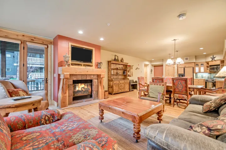 Living area featuring a stone fireplace with a wood mantle, wood-finish flooring, and a balcony access door