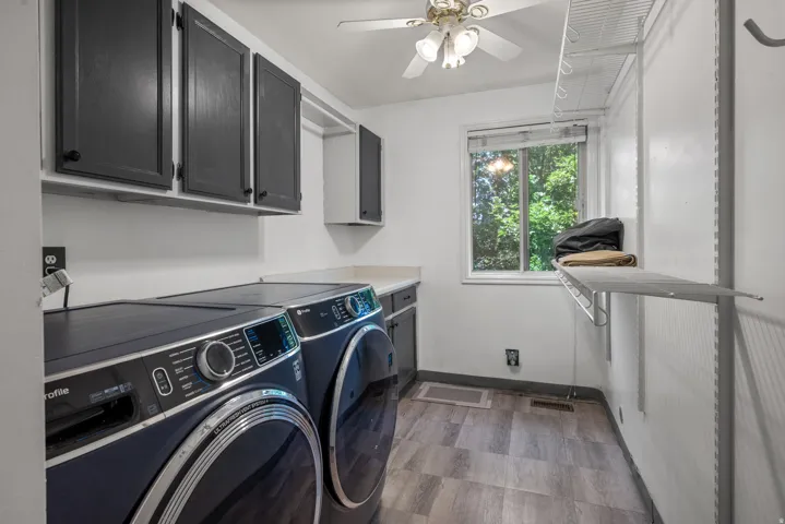 Dedicated laundry space featuring dark cabinetry, a built-in countertop, wood-finish flooring, a ceiling fan, and a window for natural light