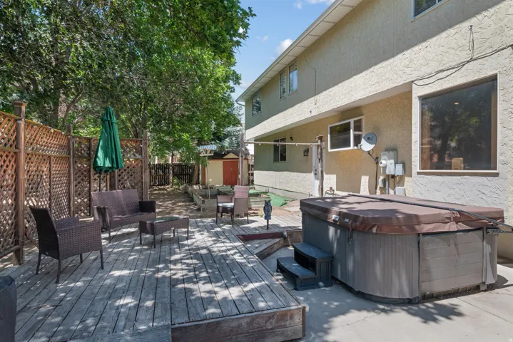 Expansive backyard featuring a large wooden deck, privacy lattice fencing, mature trees, and hot tub