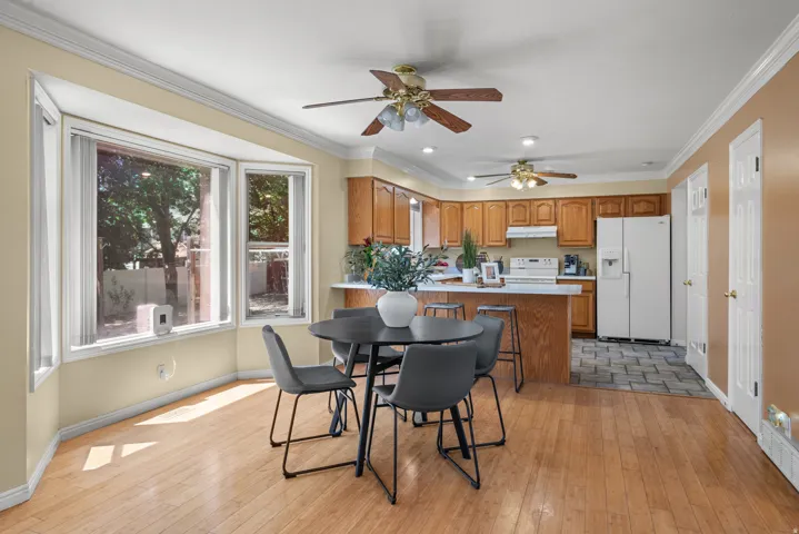 Open-concept kitchen and dining area featuring a bay window, wood-finish flooring, two ceiling fans, wood cabinetry, and a kitchen island with seating