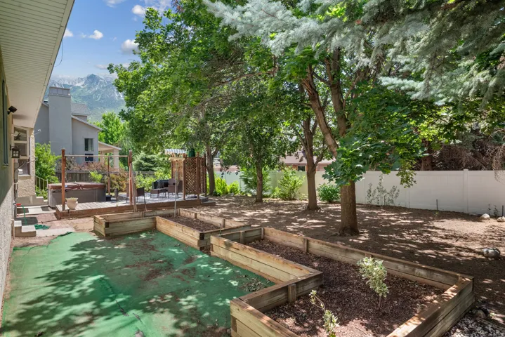 Expansive backyard featuring multiple raised garden beds, mature trees, and a privacy fence