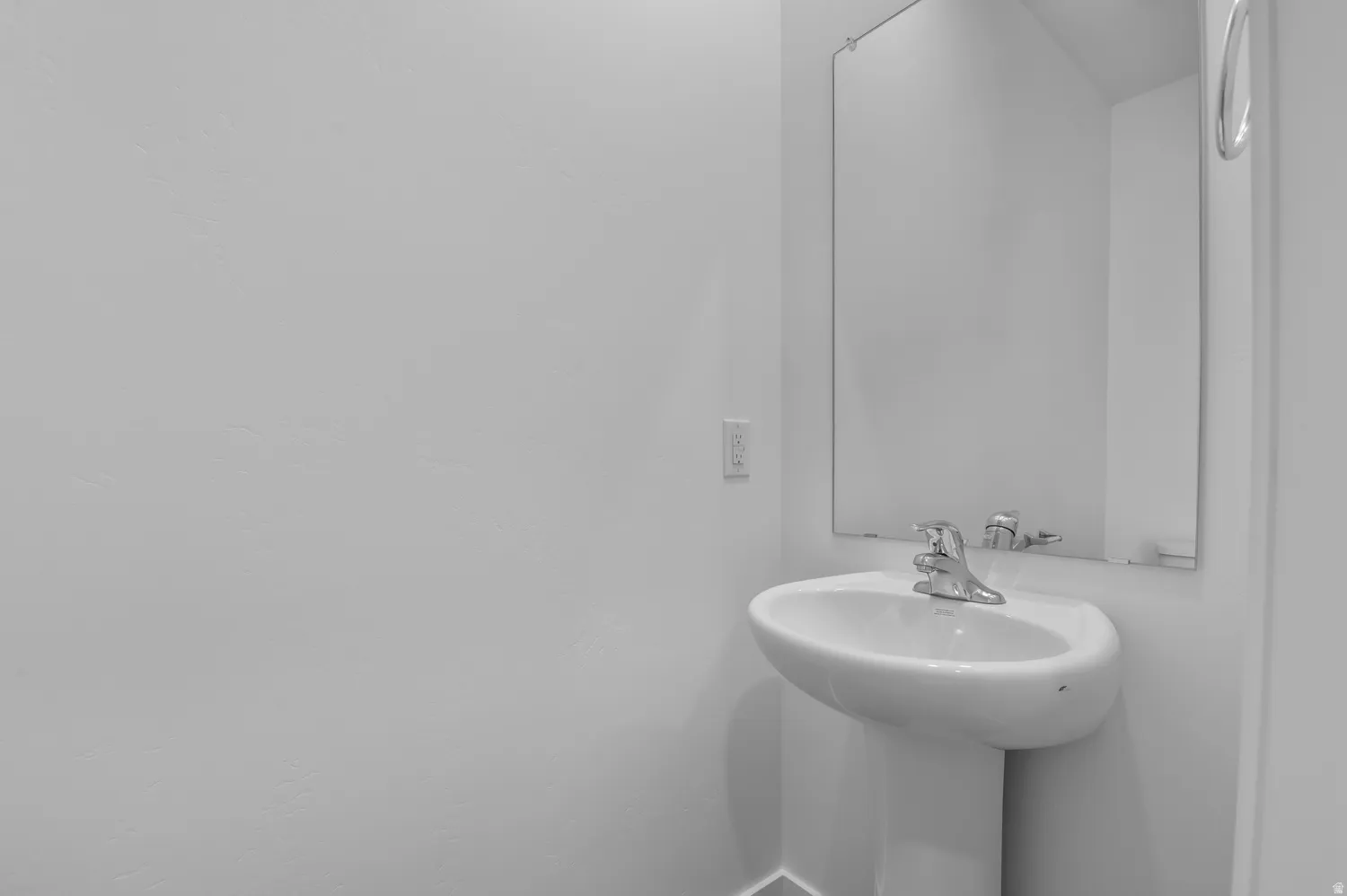 Pedestal sink with chrome faucet, complemented by a rectangular wall-mounted mirror