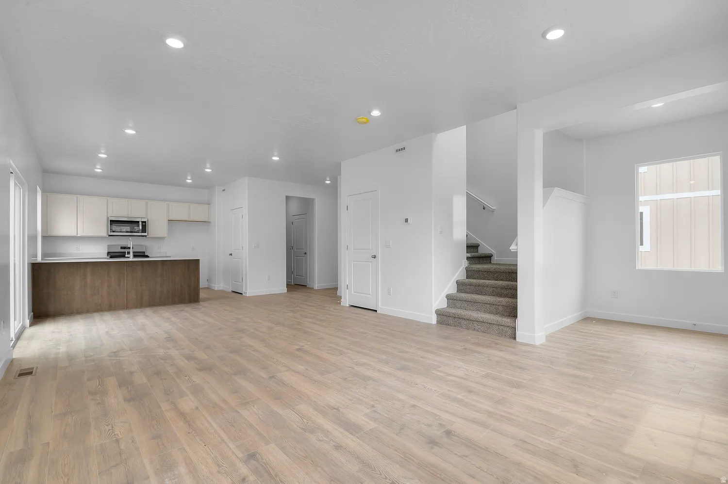 Spacious room featuring light wood-finish flooring, recessed lighting, and a modern kitchen area