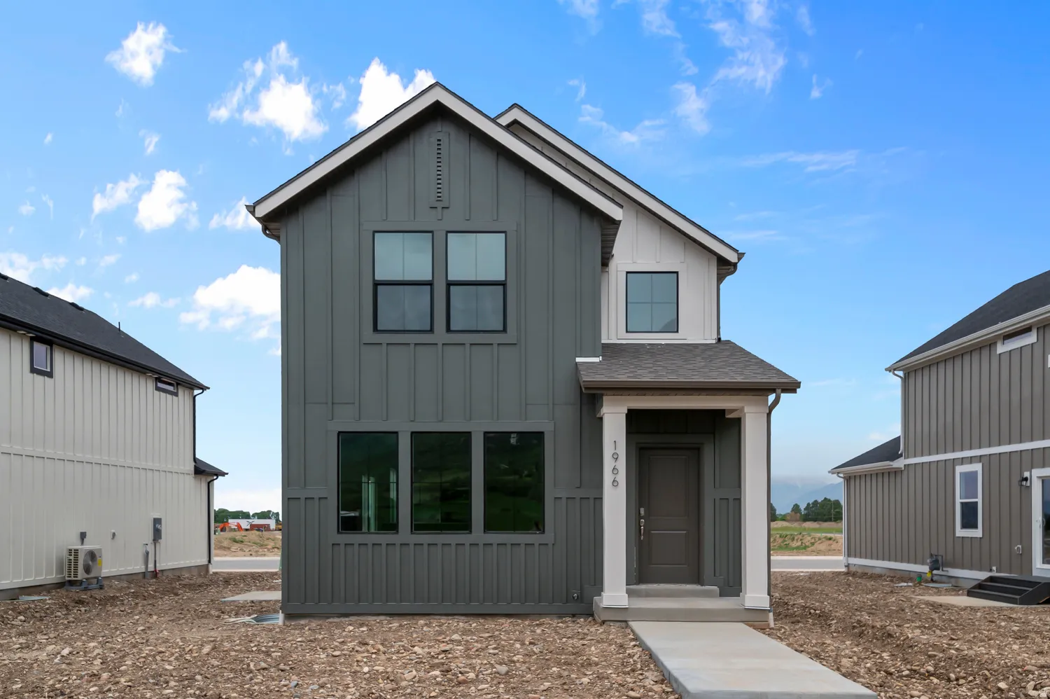 Contemporary two-story residence featuring a gray and white board and batten facade, dark trim windows, and a covered entry porch