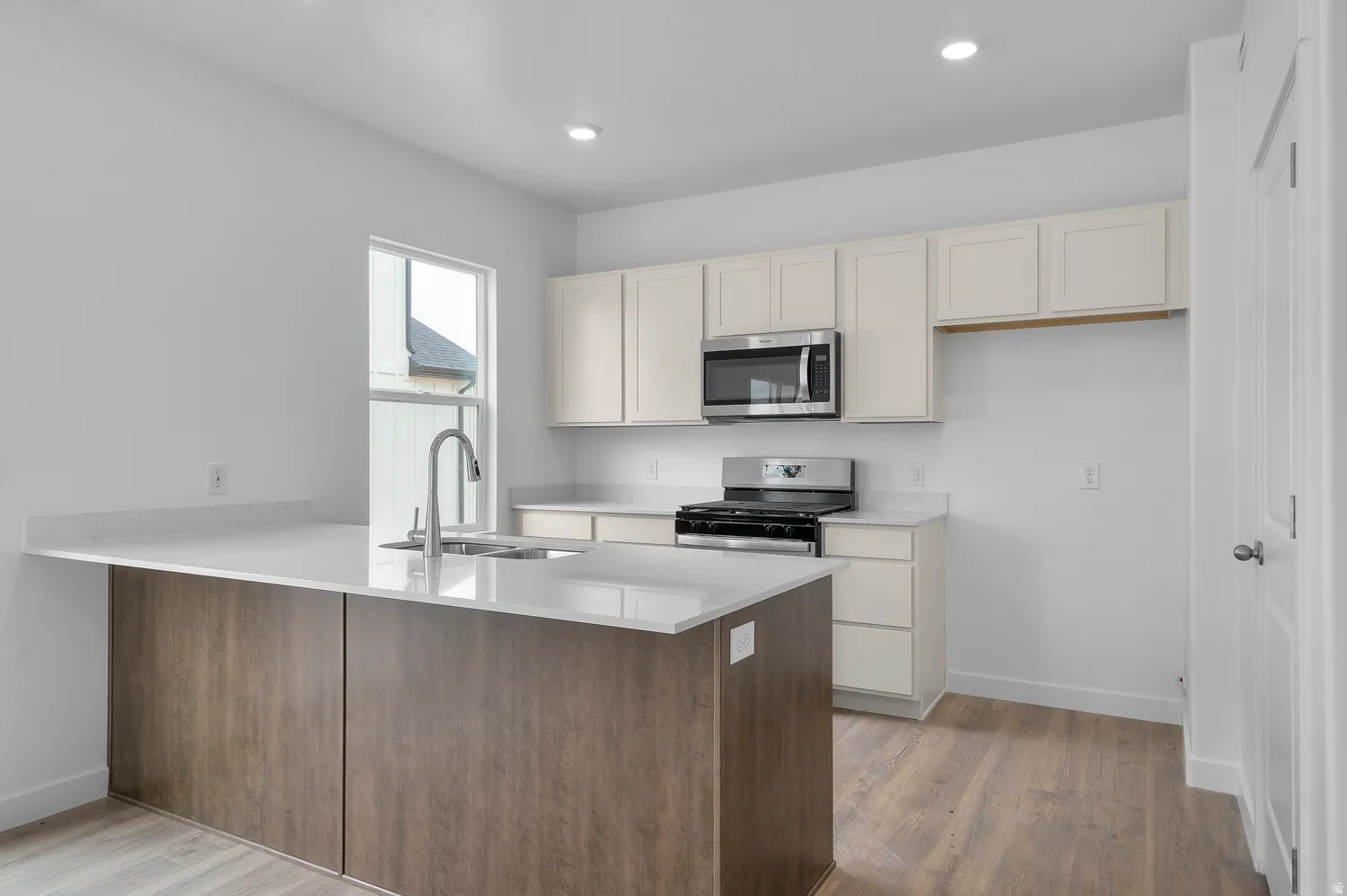 Kitchen featuring a central island with wood-finish paneling, light-colored countertops, stainless steel appliances, upper and lower cabinetry, and wood-finish flooring