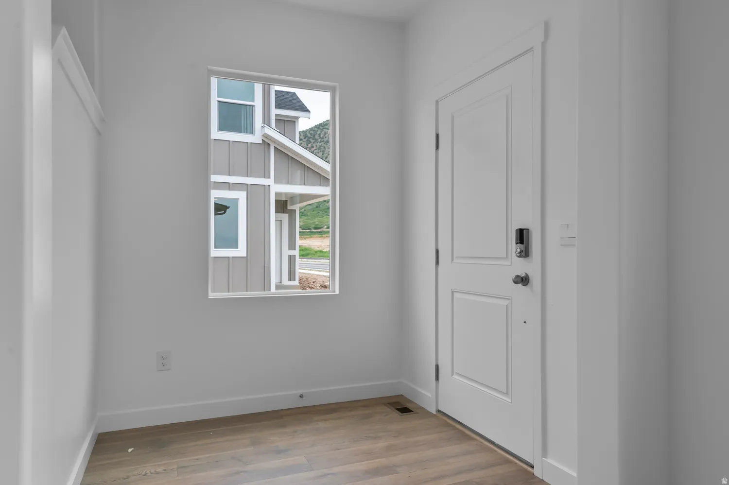 Entryway featuring a white paneled door, wood-finish flooring, a smart lock, and a window with white trim