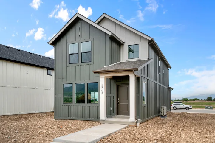 Contemporary two-story residence featuring board and batten siding, a covered entry porch, dark-framed windows, and a concrete pathway