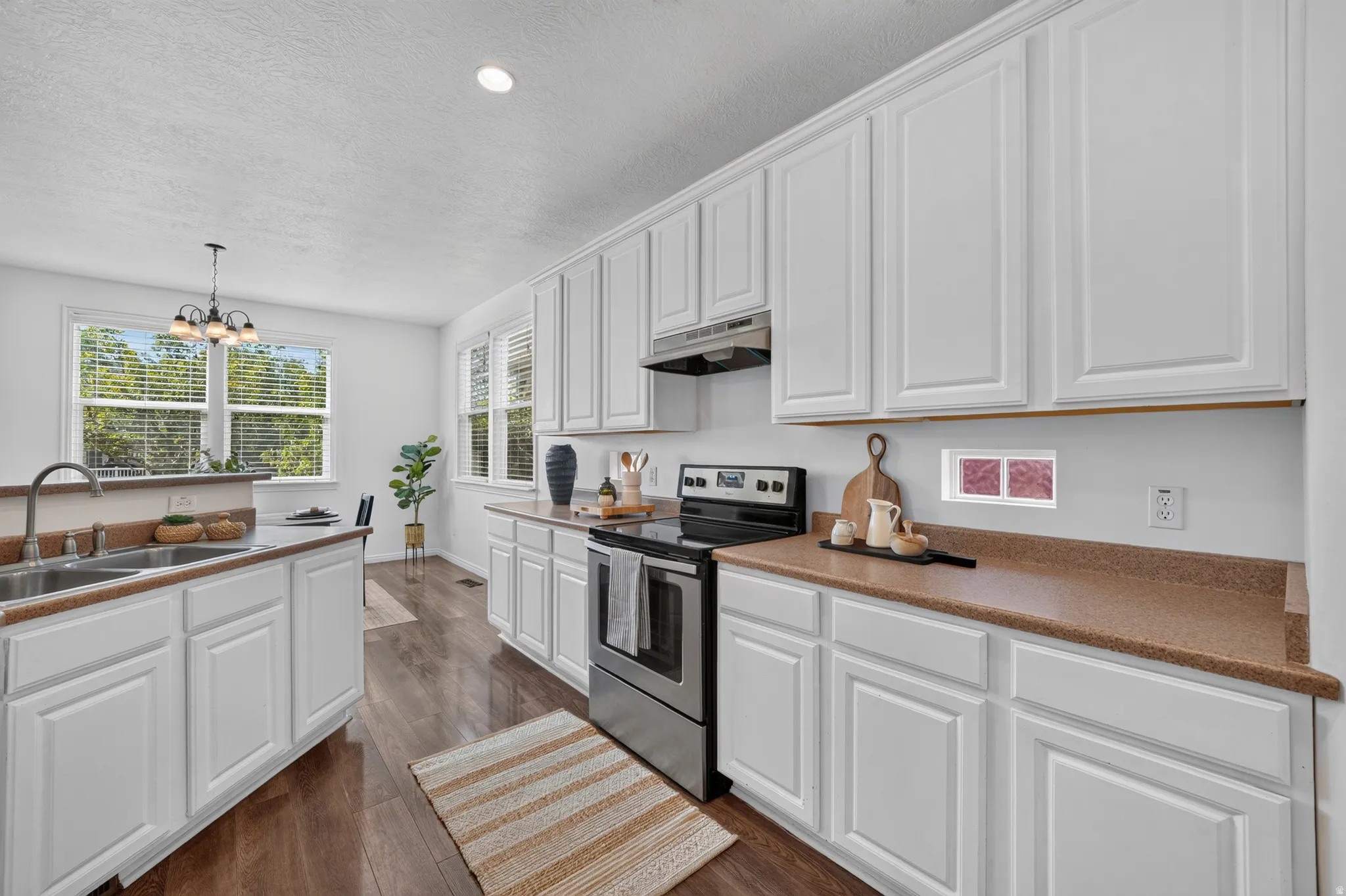 Bright kitchen featuring extensive white cabinetry, durable laminate countertops, stainless steel appliances, wood-finish flooring, and ample natural light from multiple windows