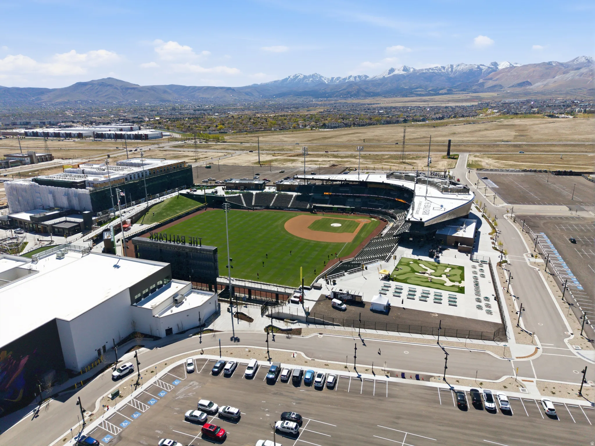Outdoor entertainment facility featuring a large, manicured athletic field, tiered stadium seating, and adjacent surface parking