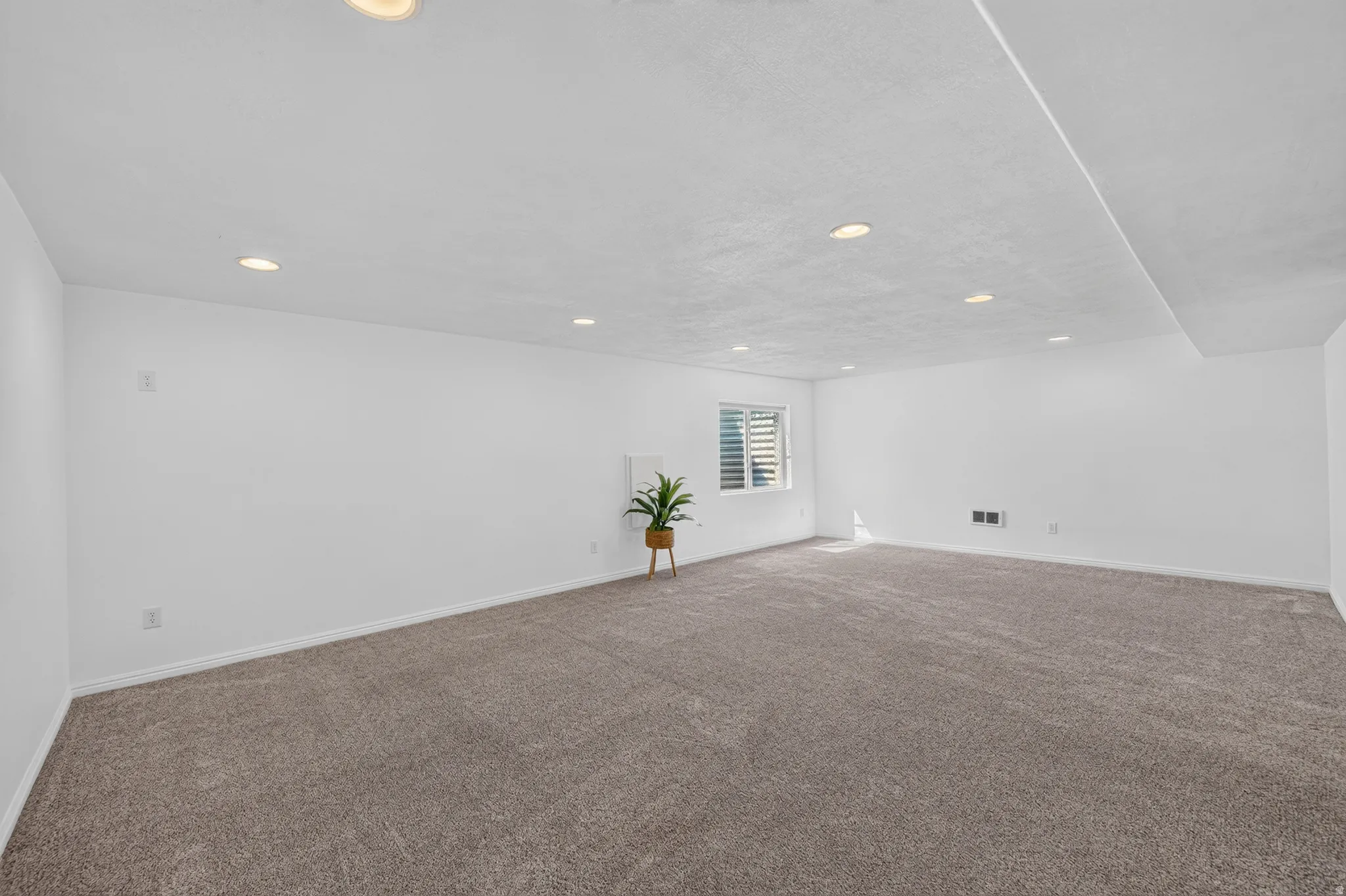 Spacious room featuring neutral carpeting, white walls, recessed lighting, and a window with horizontal blinds