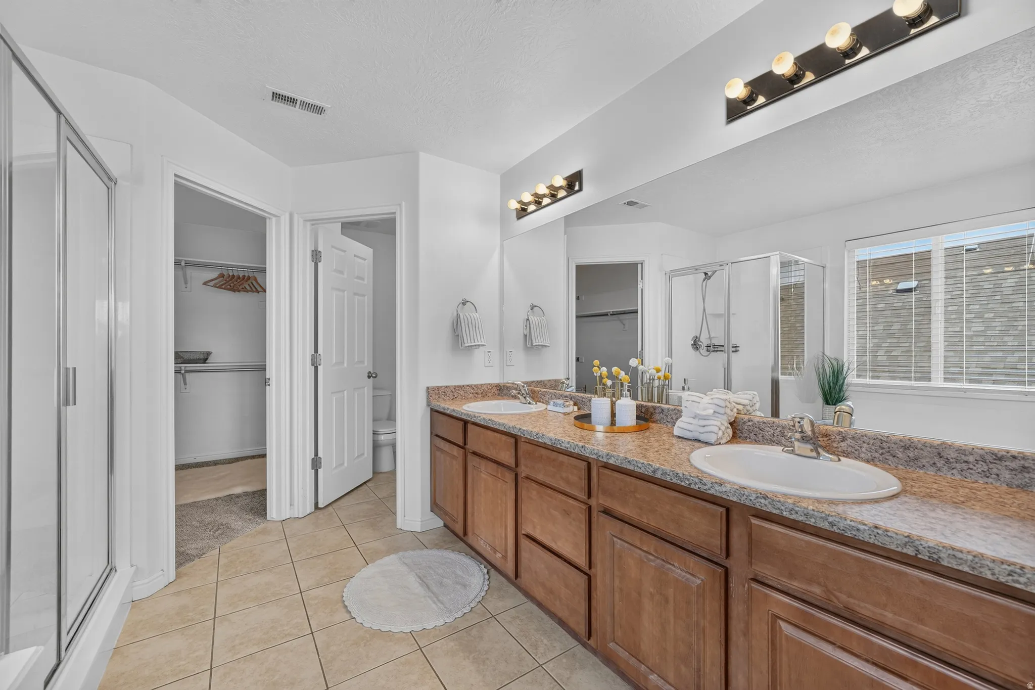 Dual vanity with wood-finish cabinetry, speckled countertop, and integrated sinks