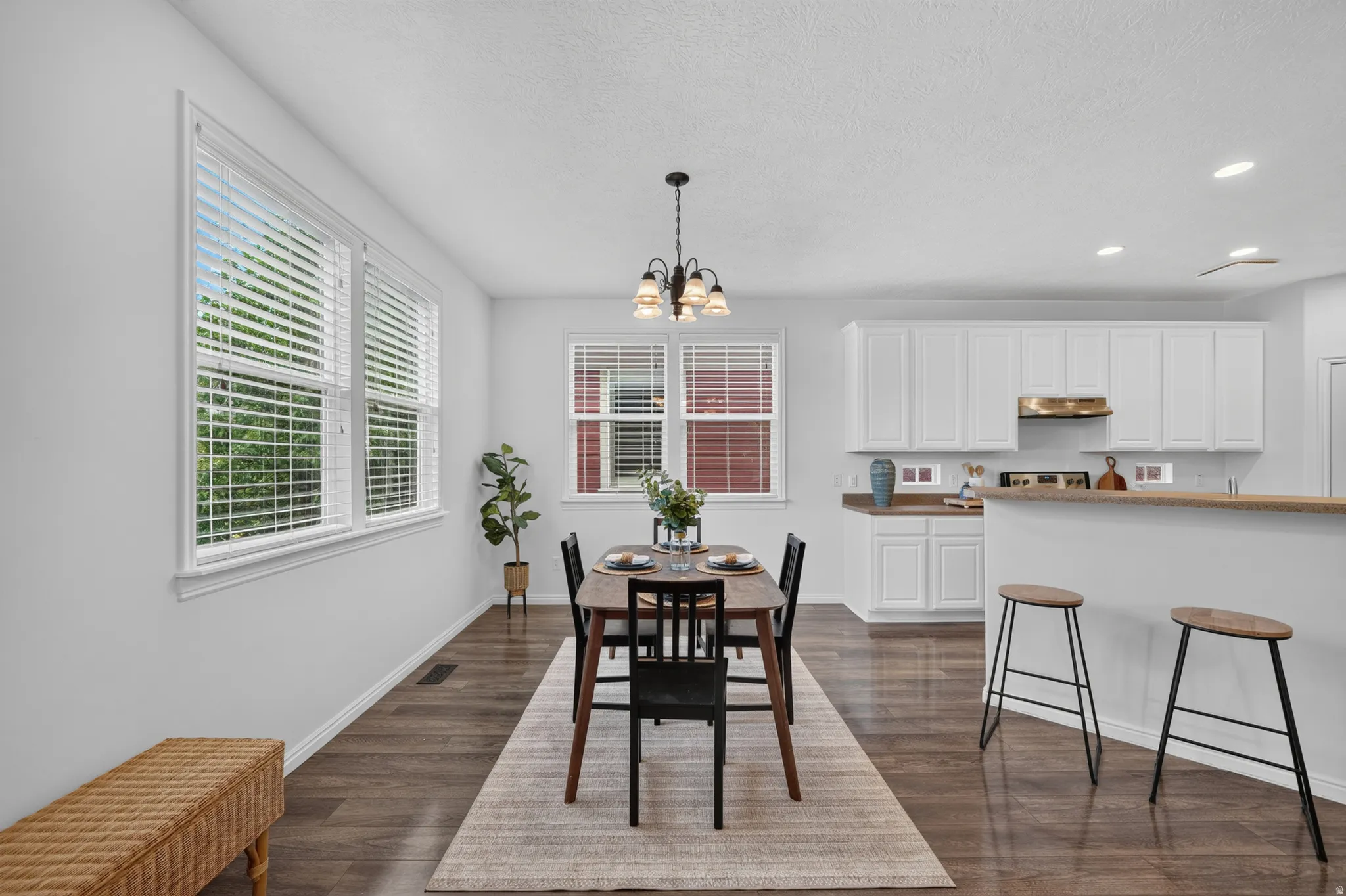 Open-concept dining area featuring wood-finish flooring, multiple windows with blinds, and a chandelier