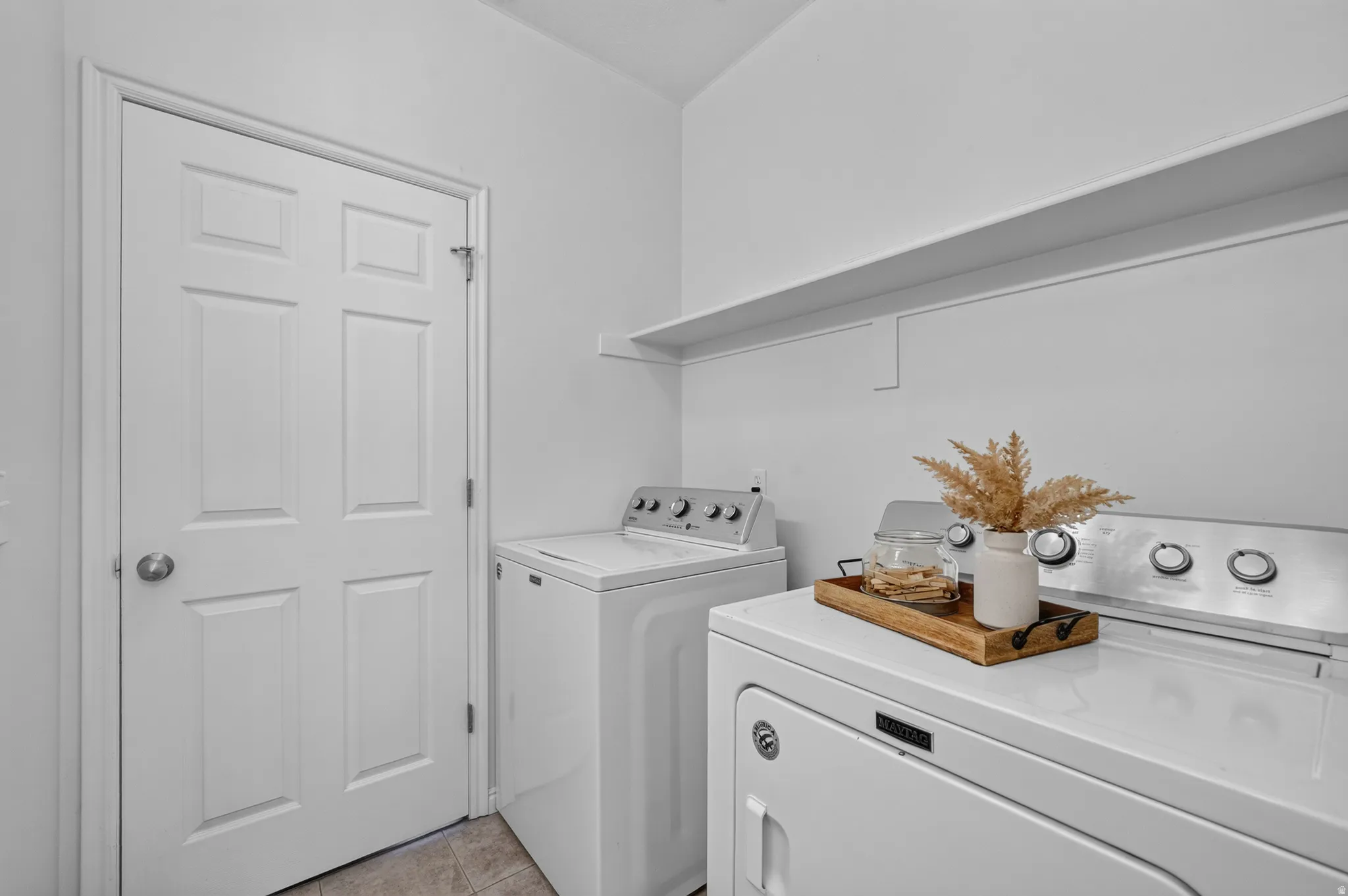 Dedicated laundry area featuring a white six-panel door, built-in wall shelving, and tile flooring