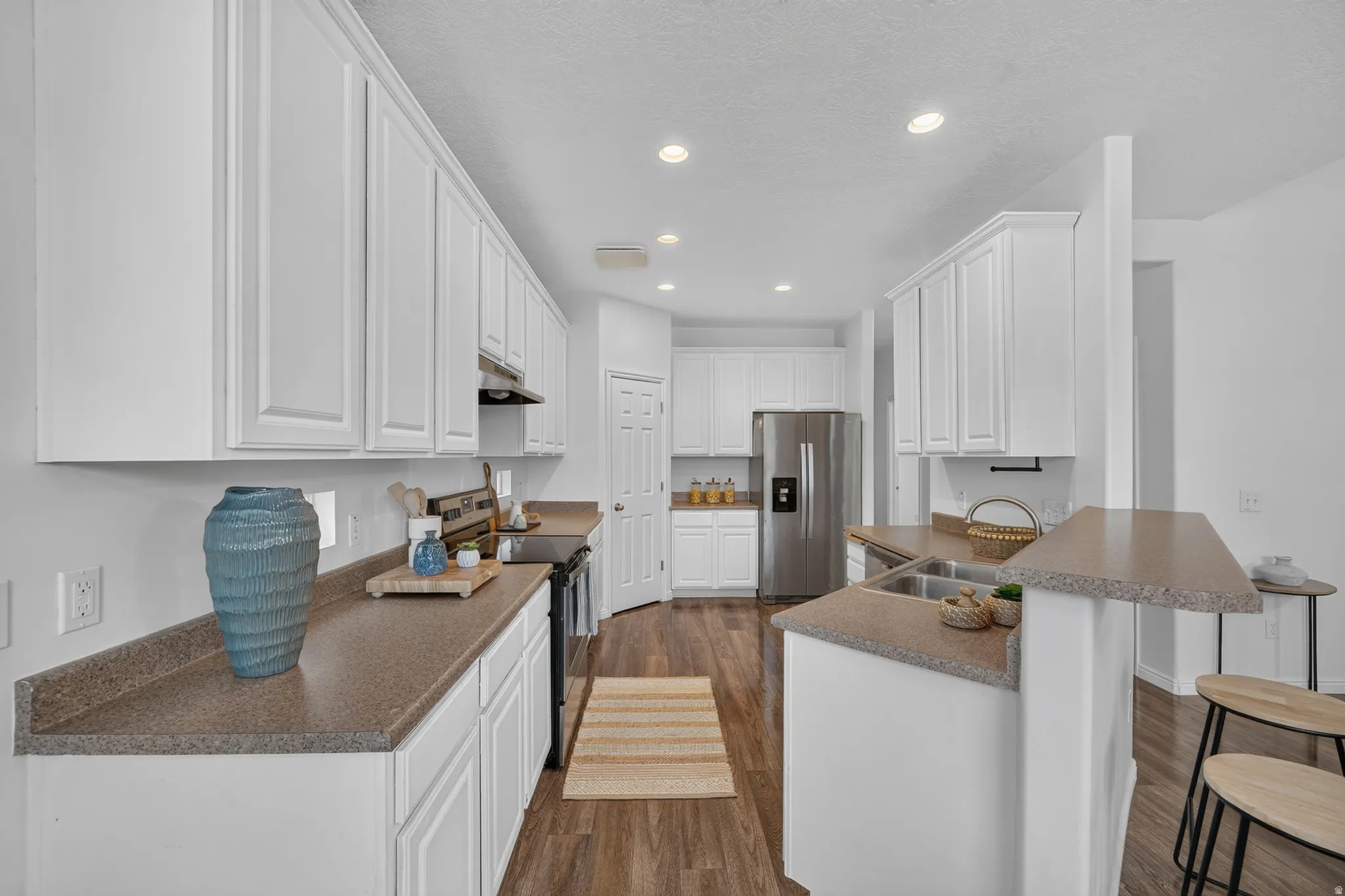 Kitchen featuring extensive white cabinetry, wood-finish flooring, a stainless steel refrigerator, and composite countertops